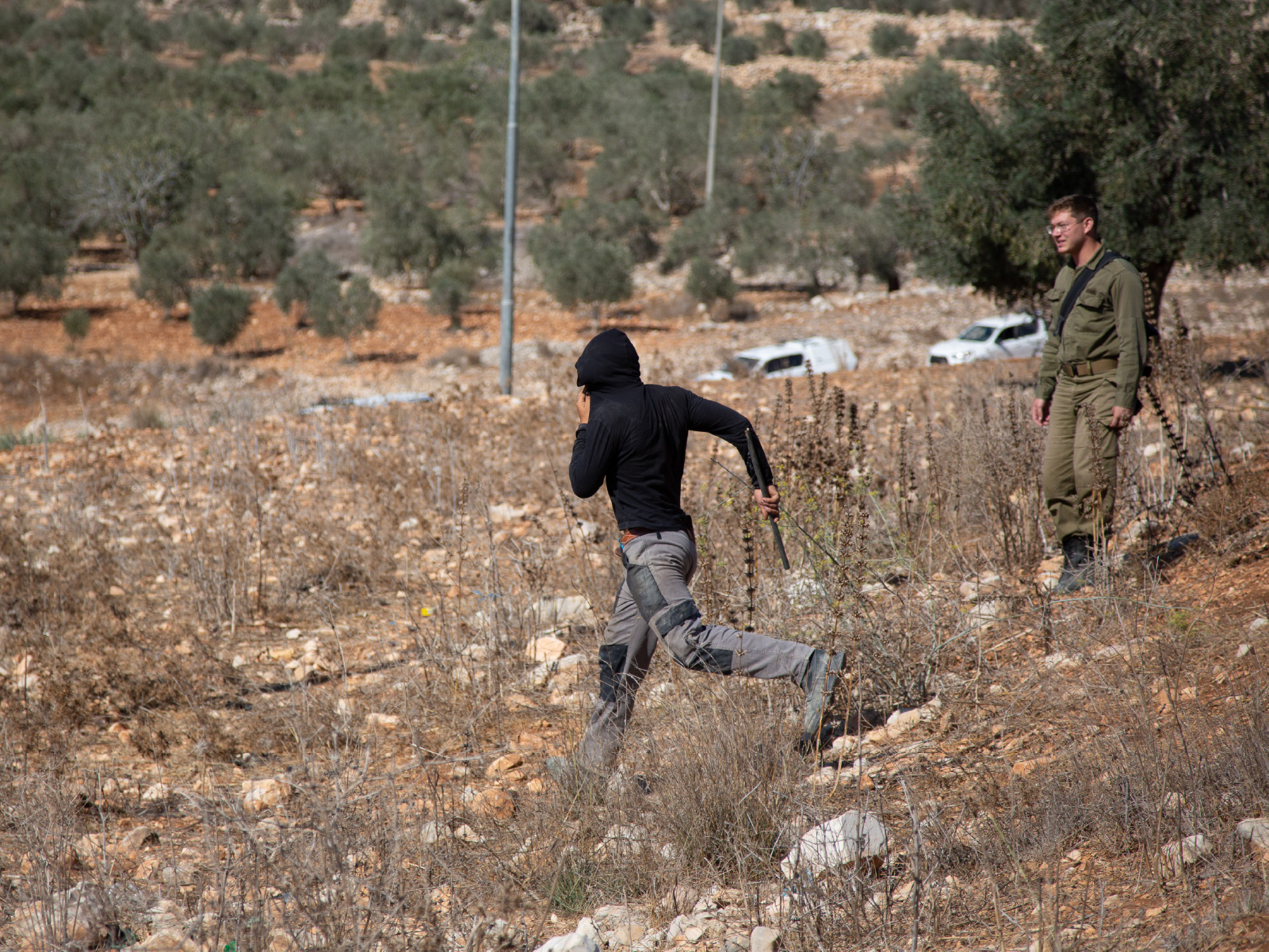 INTERACTIVE - Teenage settler running after Palestinian in Deir Ammar as soldier looks on-1764686010