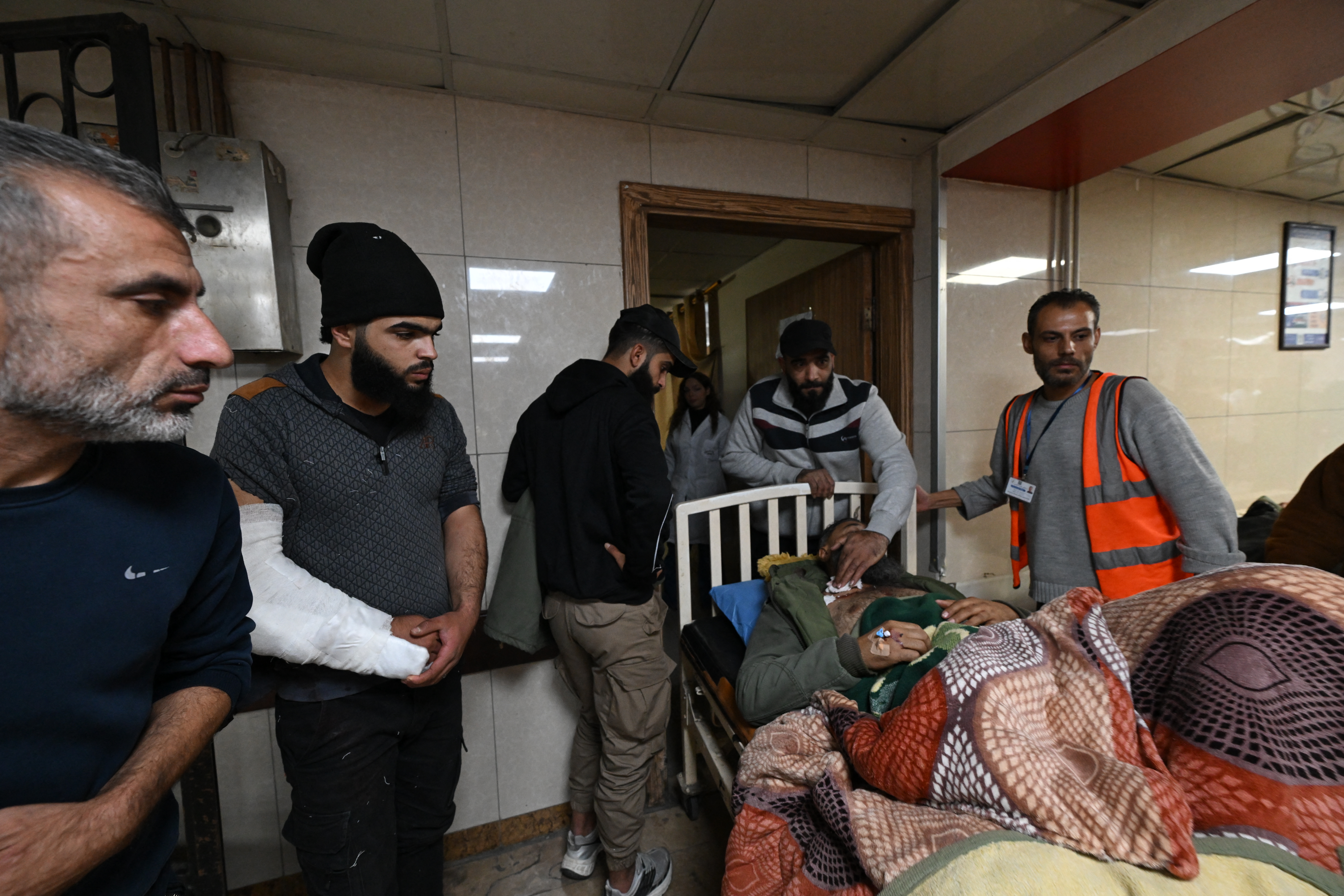 People stand next to a wounded man lying on a hospital bed at Al-Mouwasat Hospital in Damascus, following a operation by Israeli forces in the Syrian village of Beit Jin on November 28, 2025.