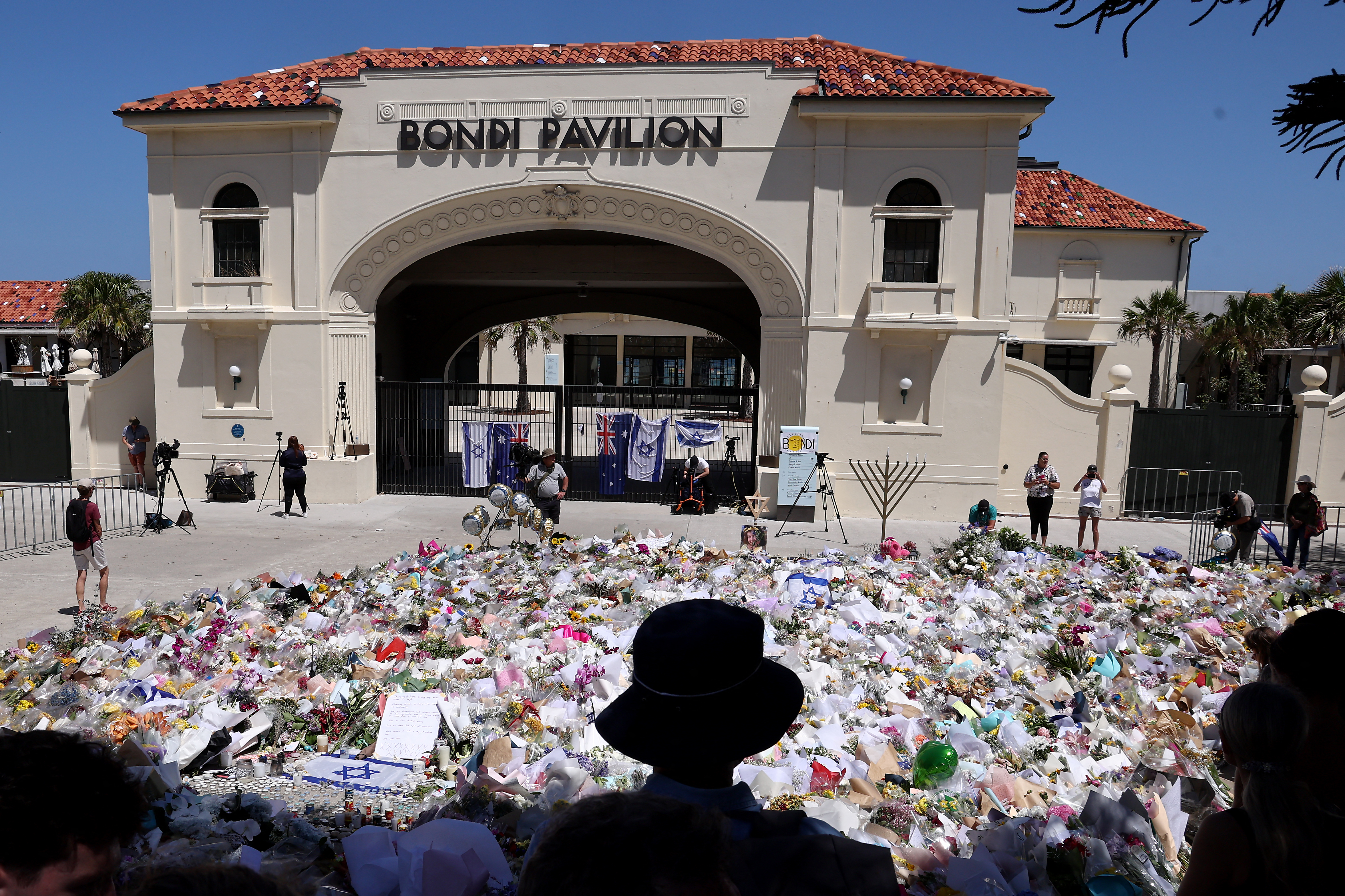 Mourners stand near tributes piled together.