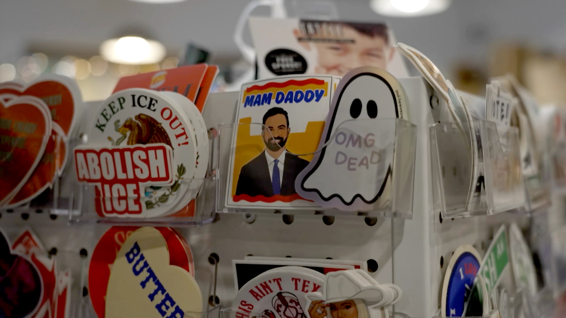 A Zohran Mamdani "Mam Daddy" sticker sits next to "Abolish ICE" and other politically themed merchandise on sale in New York City. [Al Jazeera]