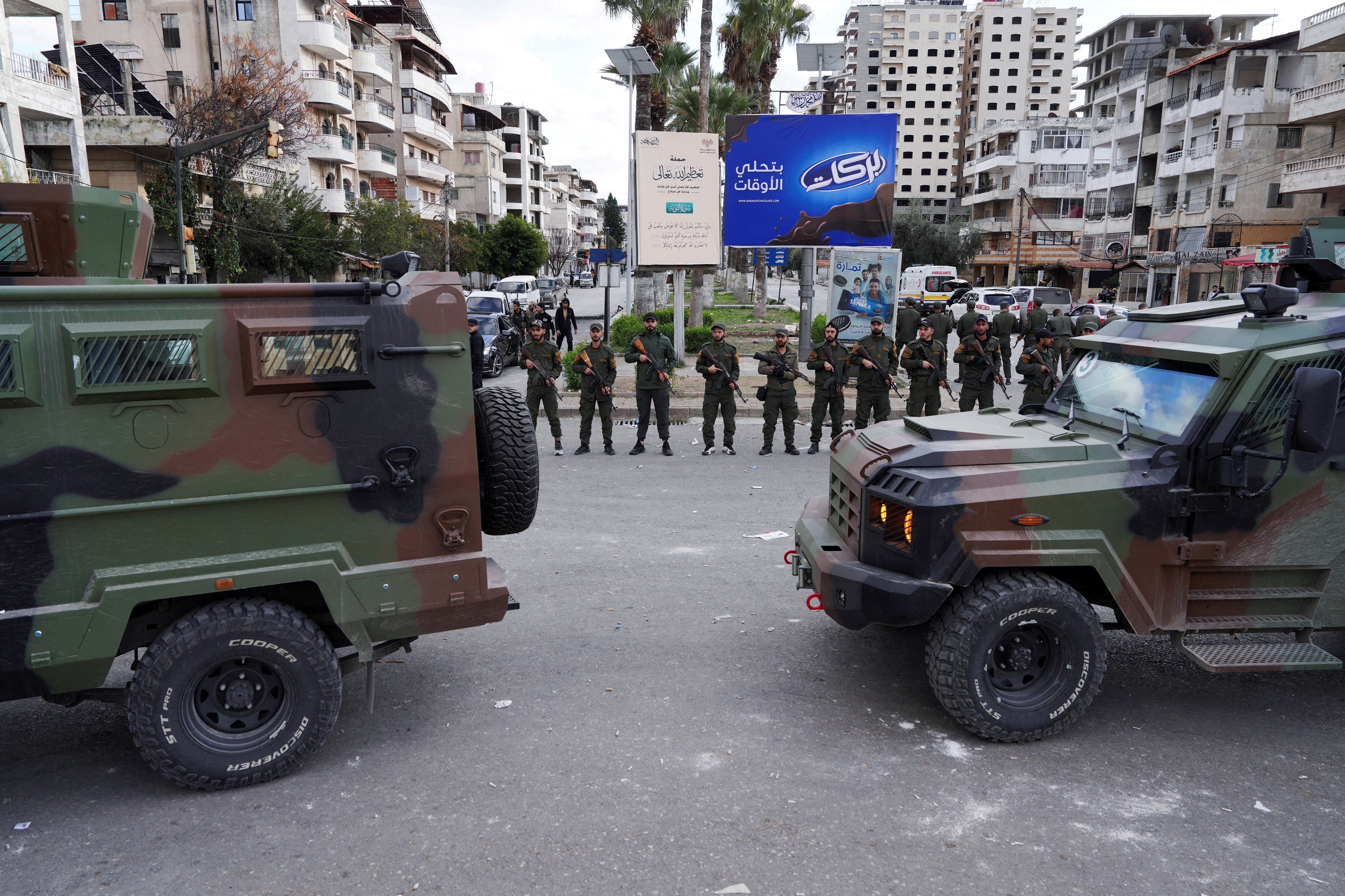 FILE PHOTO: Members of the Syrian Security forces stand guard near military vehicles on the day people from the Alawite sect protest as they demand federalism and an end to what they say is the killing and violations against Alawites, in Latakia, Syria, December 28, 2025. REUTERS/Karam al-Masri/File Photo