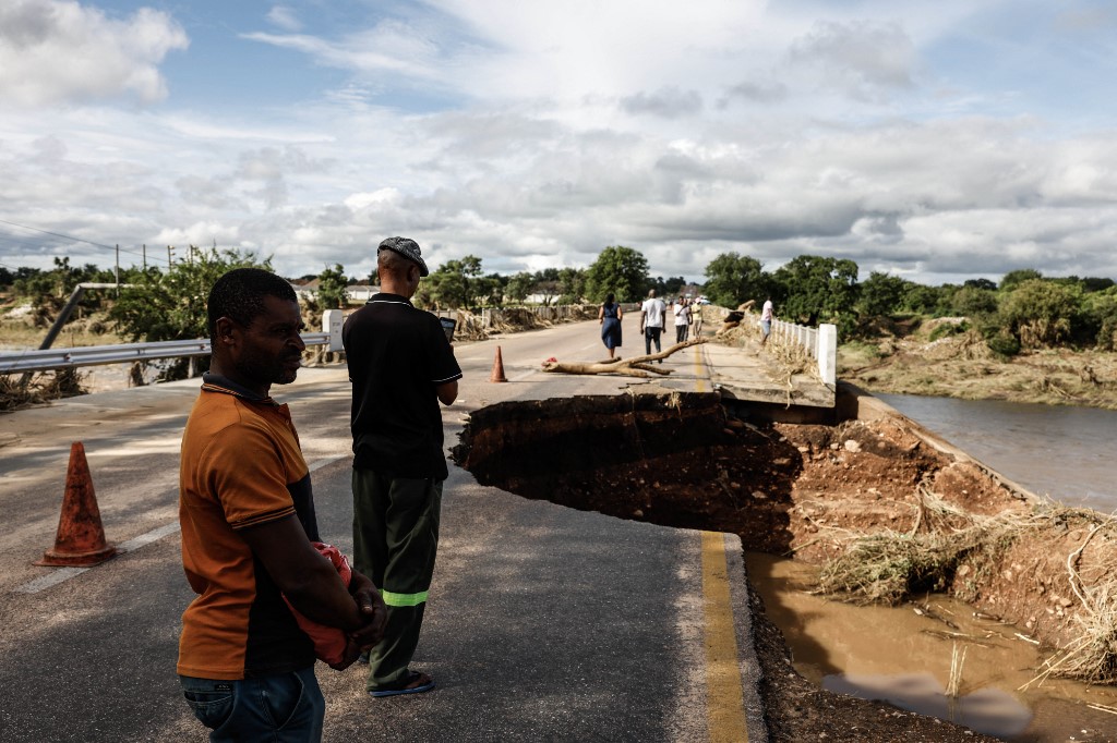 Onlookers inspect damage to a bridge over a river.
