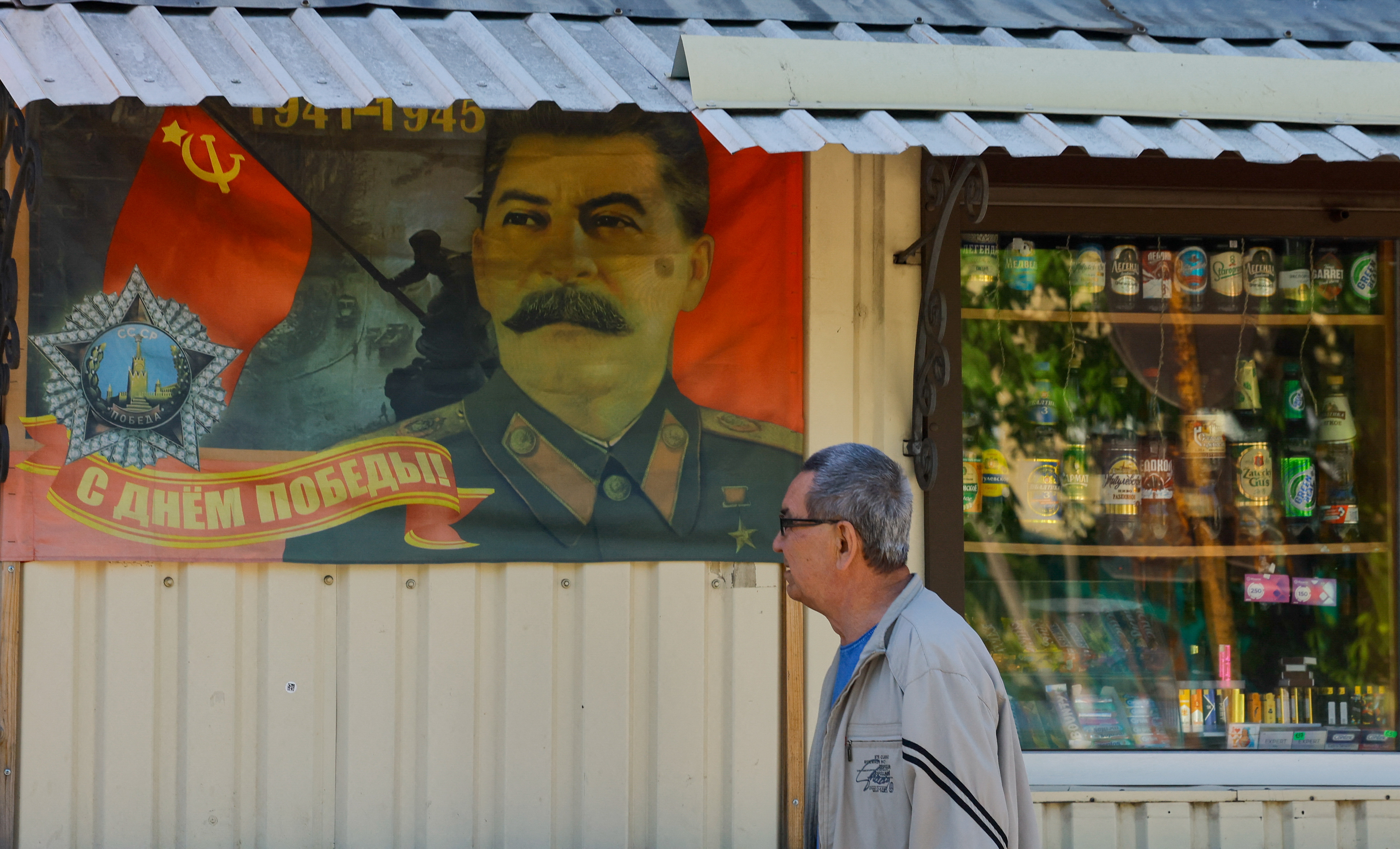 A man walks past a poster displaying a portrait of Soviet leader Joseph Stalin and an illustration of a Red Army soldier raising a flag atop the Reichstag.