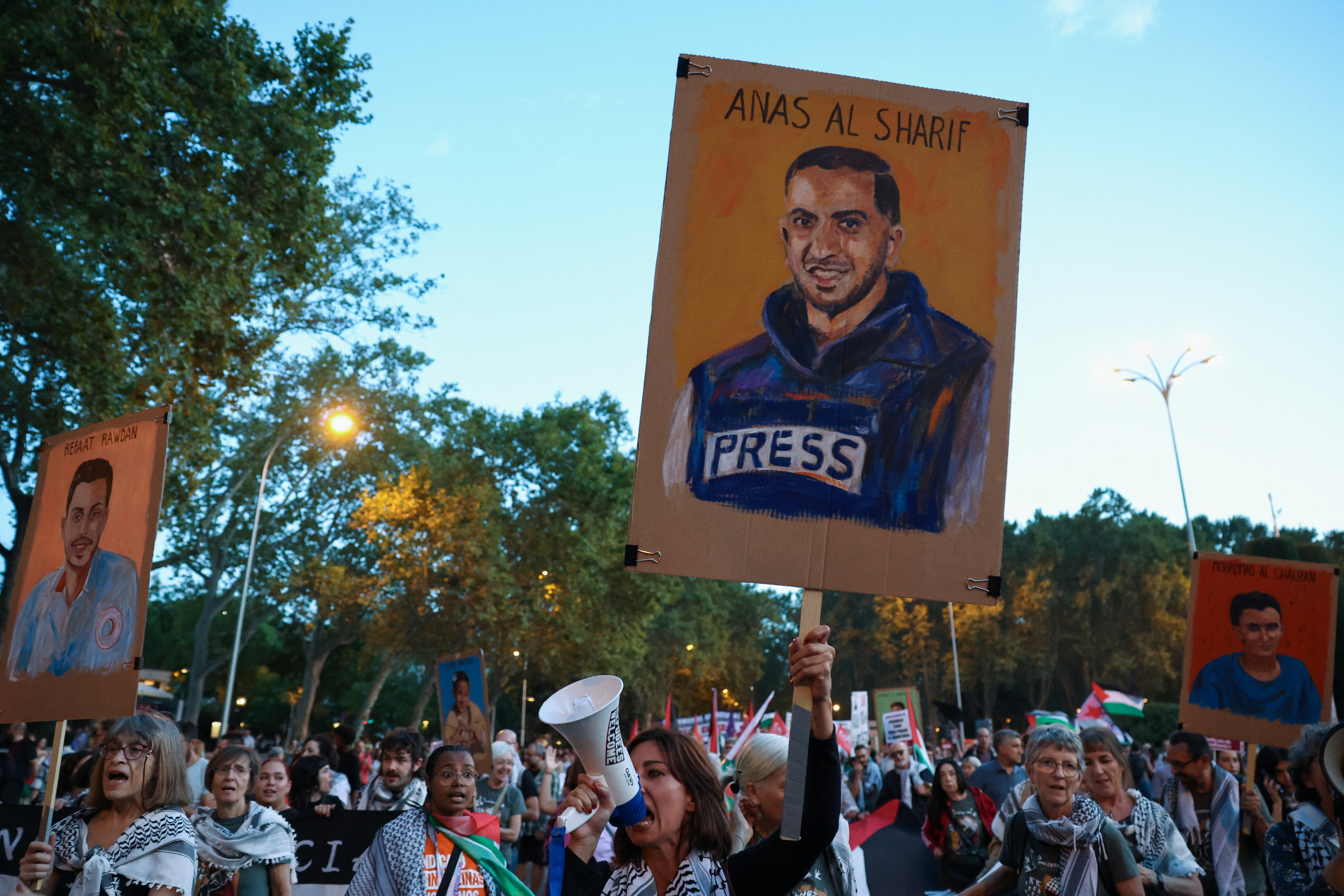 A woman displays a memorial sign of slain Palestinian Al Jazeera journalist Anas al-Sharif as people demonstrate.