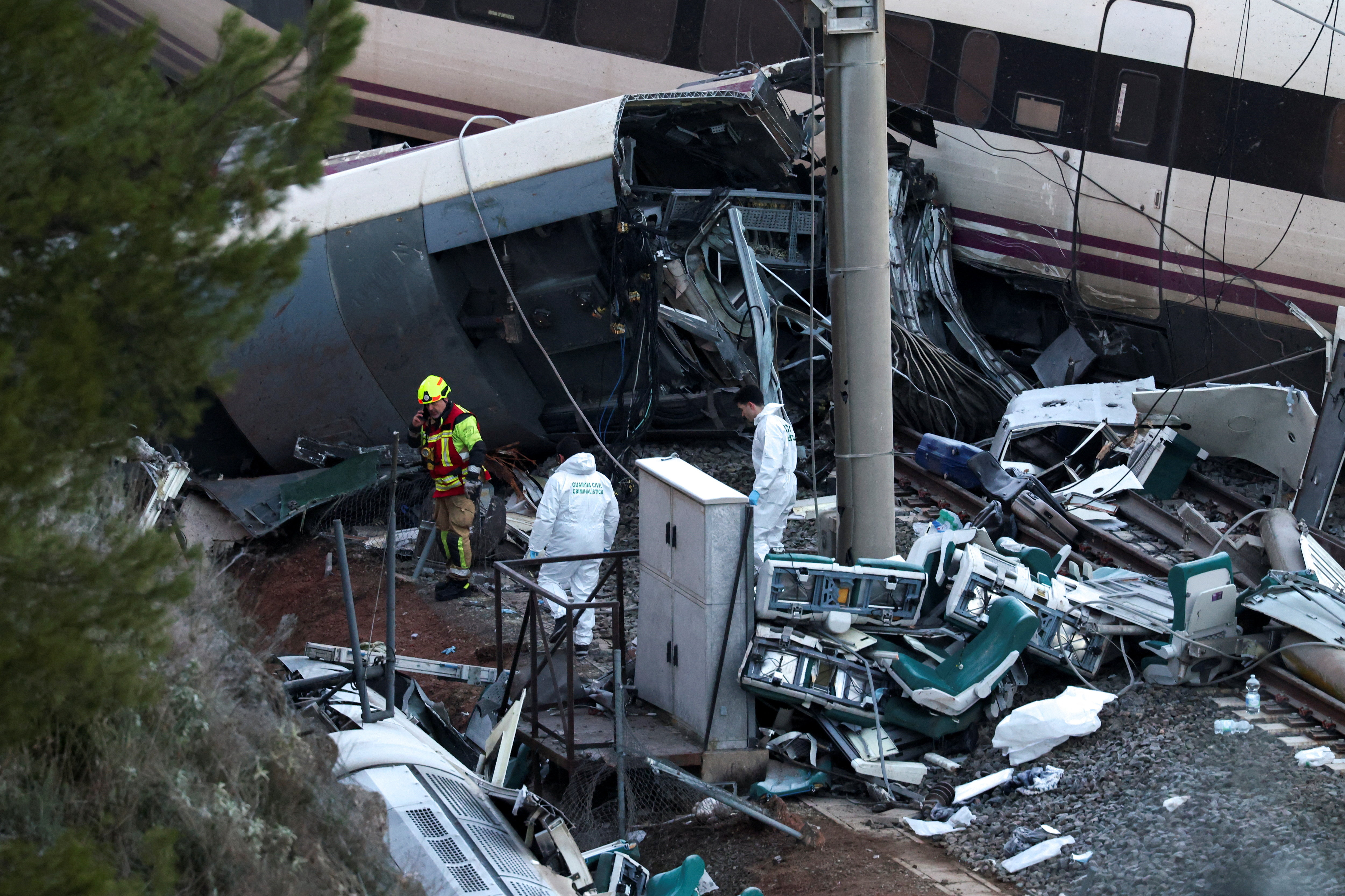 A firefighter and members of the Spanish Civil Guard work next to one of the trains involved in the accident, at the site of a deadly derailment of two high-speed trains near Adamuz, in Cordoba, Spain, January 19, 2026. REUTERS/Susana Vera