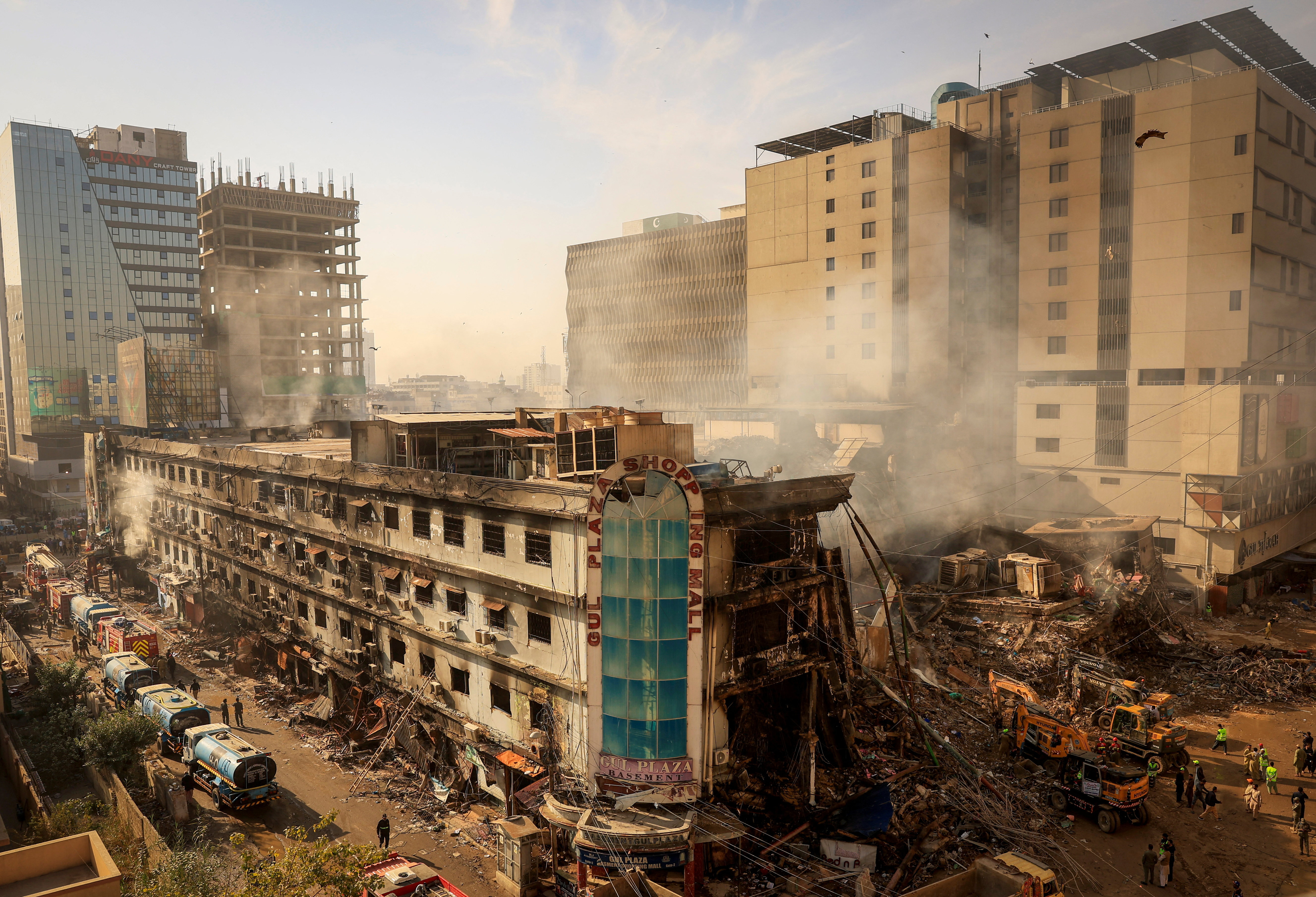 Fire department and municipal workers stand near the site, following a massive fire that broke out in the Gul Plaza Shopping Mall in Karachi, Pakistan, January 20, 2026. REUTERS/Akhtar Soomro