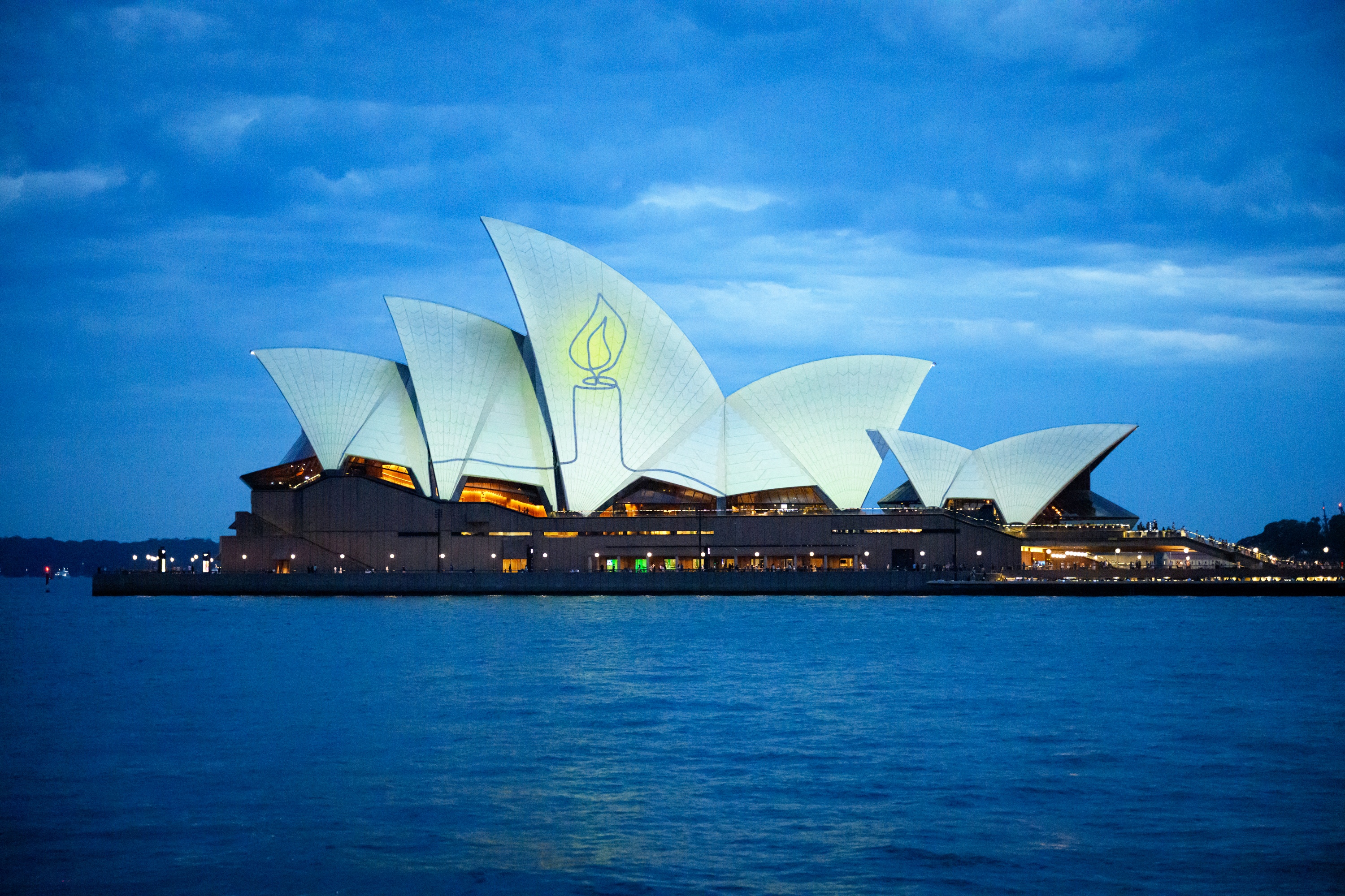 The Sydney Opera House is illuminated with candlelights in Sydney on December 21, 2025, as part of a national day of reflection honouring the victims of the Bondi Beach terrorist attack. Australians fell silent in flickering candlelight to honour the Bondi Beach shooting victims, marking one week since gunmen fired into crowds at a Jewish festival. (Photo by GEORGE CHAN / AFP)