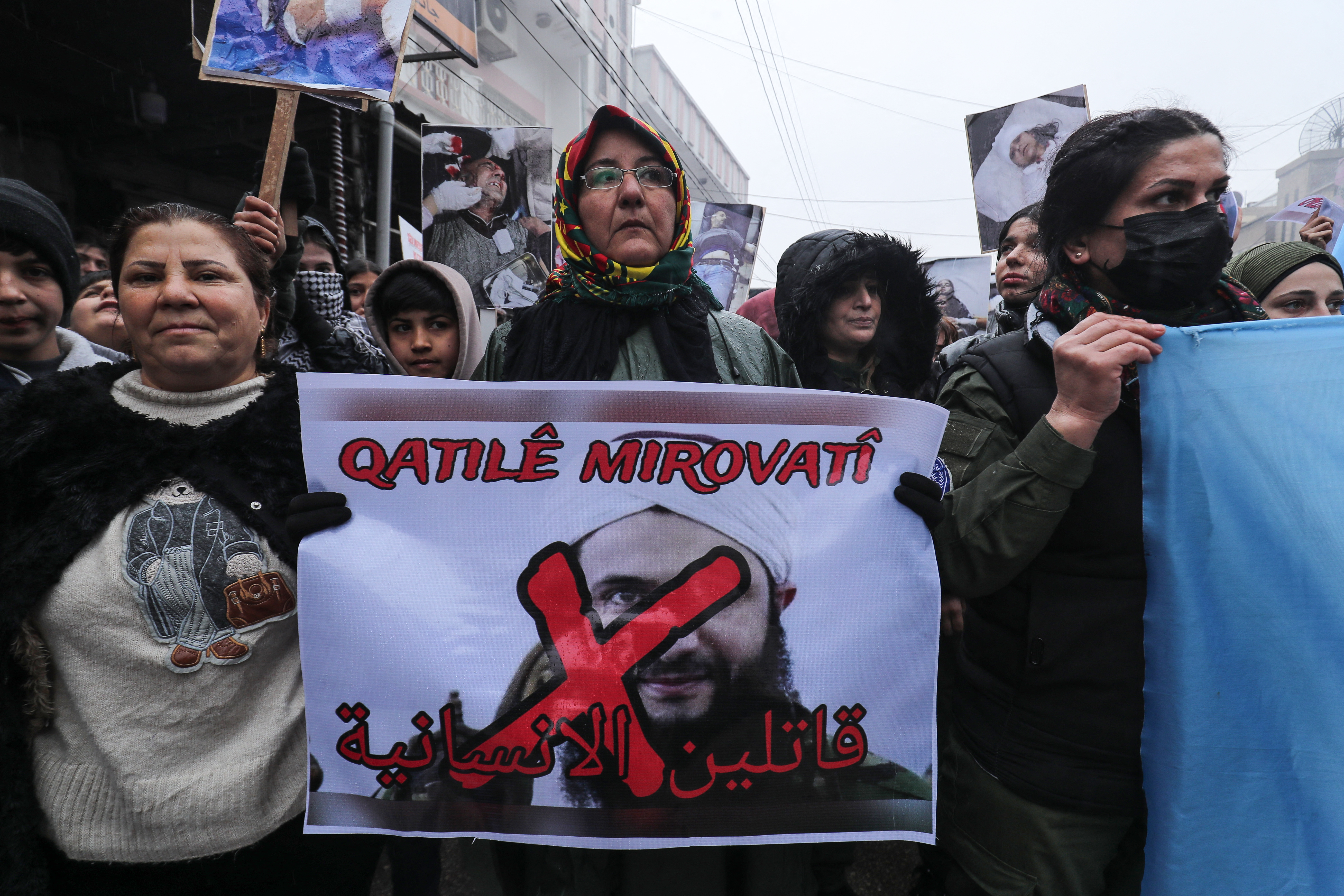 Syrian Kurds hold a portrait of Syrian President Ahmed al-Sharaa which reads "Killers of Humanity" during a protest in the Kurdish-controlled northeastern city of Qamishli on January 13, 2026, against violence they say was committed by Syrian government forces during recent clashes in Aleppo's Kurdish neighbourhoods. On the weekend, Syria's government took full control of Aleppo city after taking over its Kurdish neighbourhoods and evacuating fighters there to Kurdish-controlled areas in the country's northeast following days of clashes. (Photo by Delil SOULEIMAN / AFP)