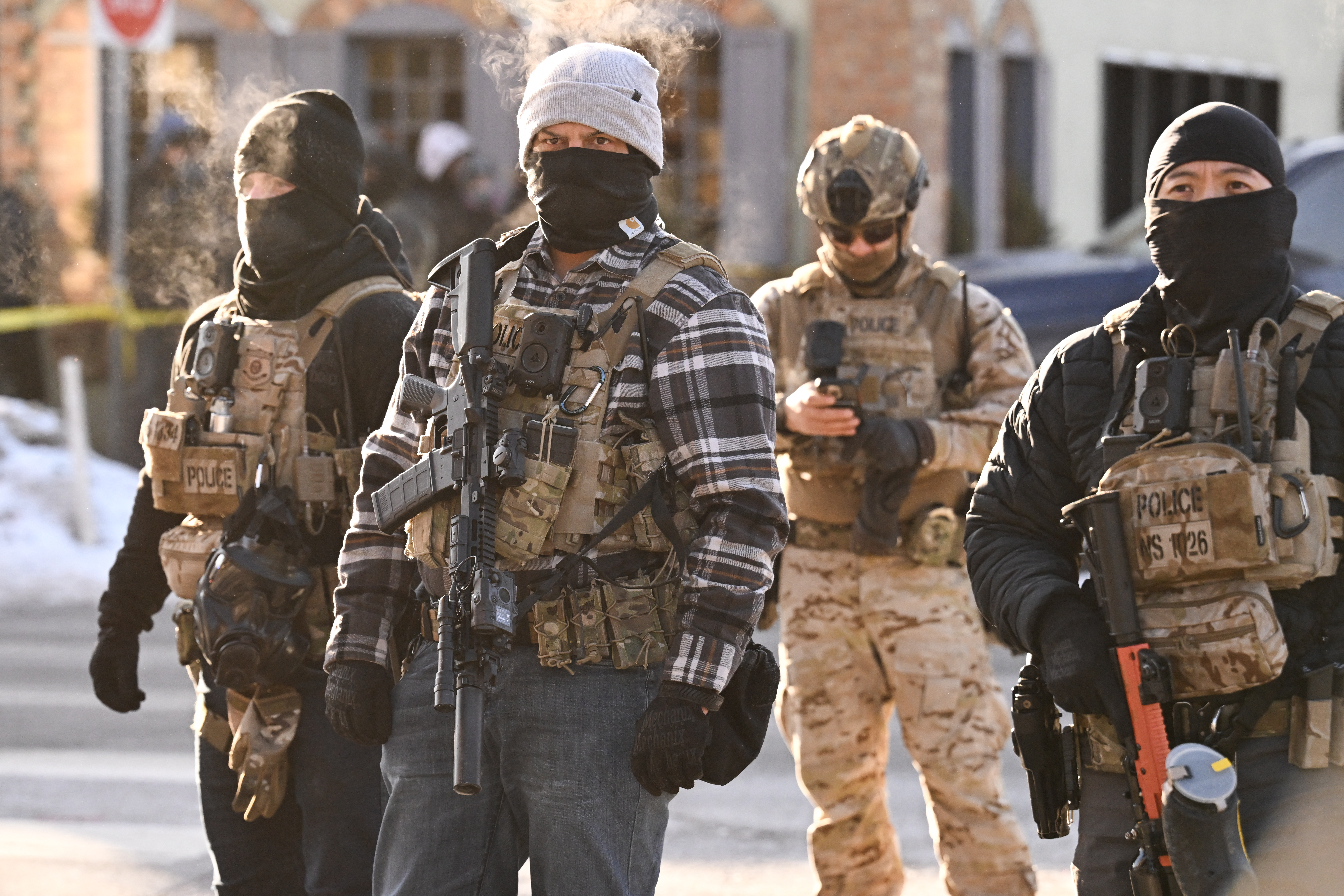 Federal agents look on as demonstrators gather near the site of where state and local authorities say a man was shot by US agents earlier in the morning in Minneapolis, Minnesota