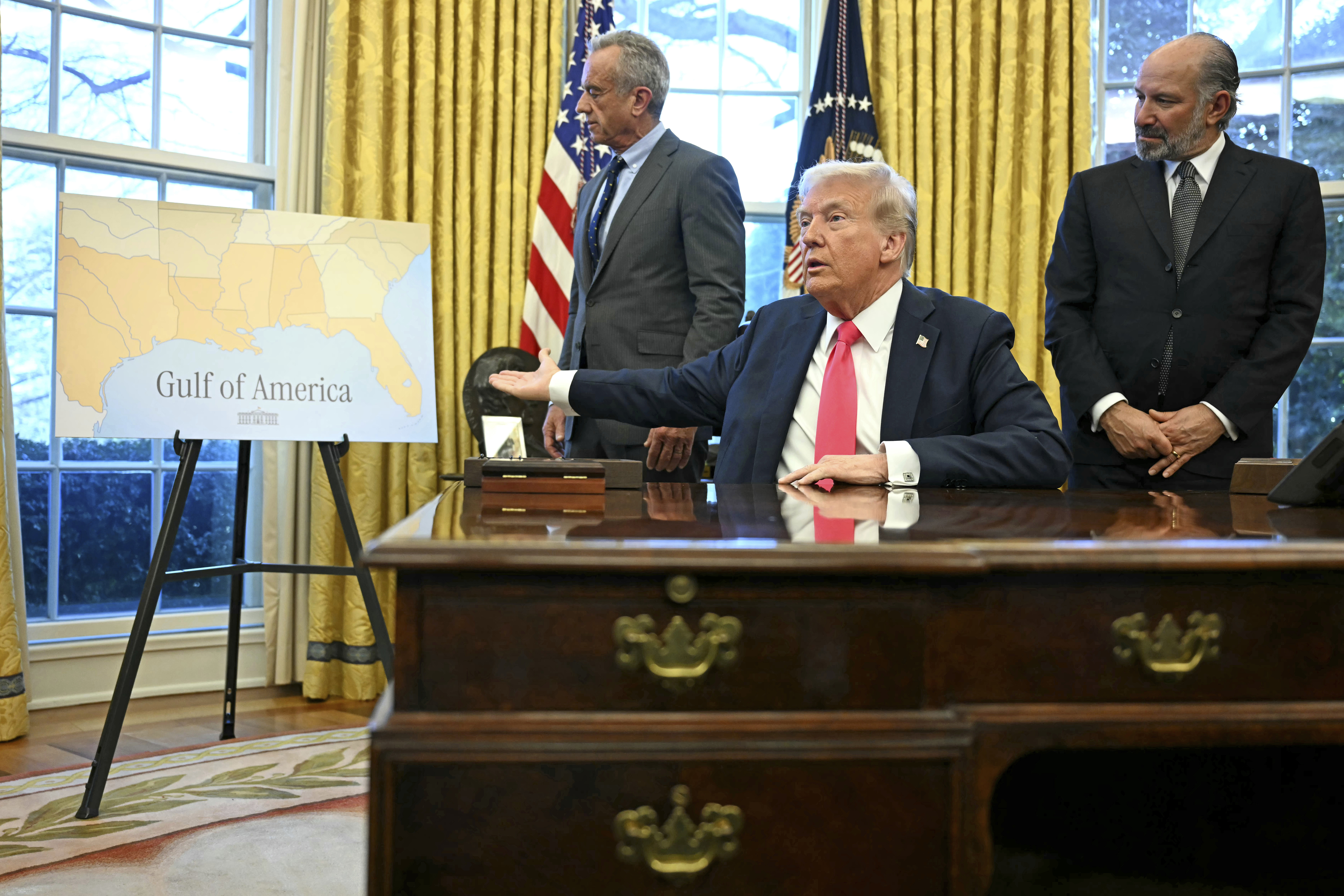 Donald Trump sits behind Oval Office desk and points to a sign that says "Gulf of America"