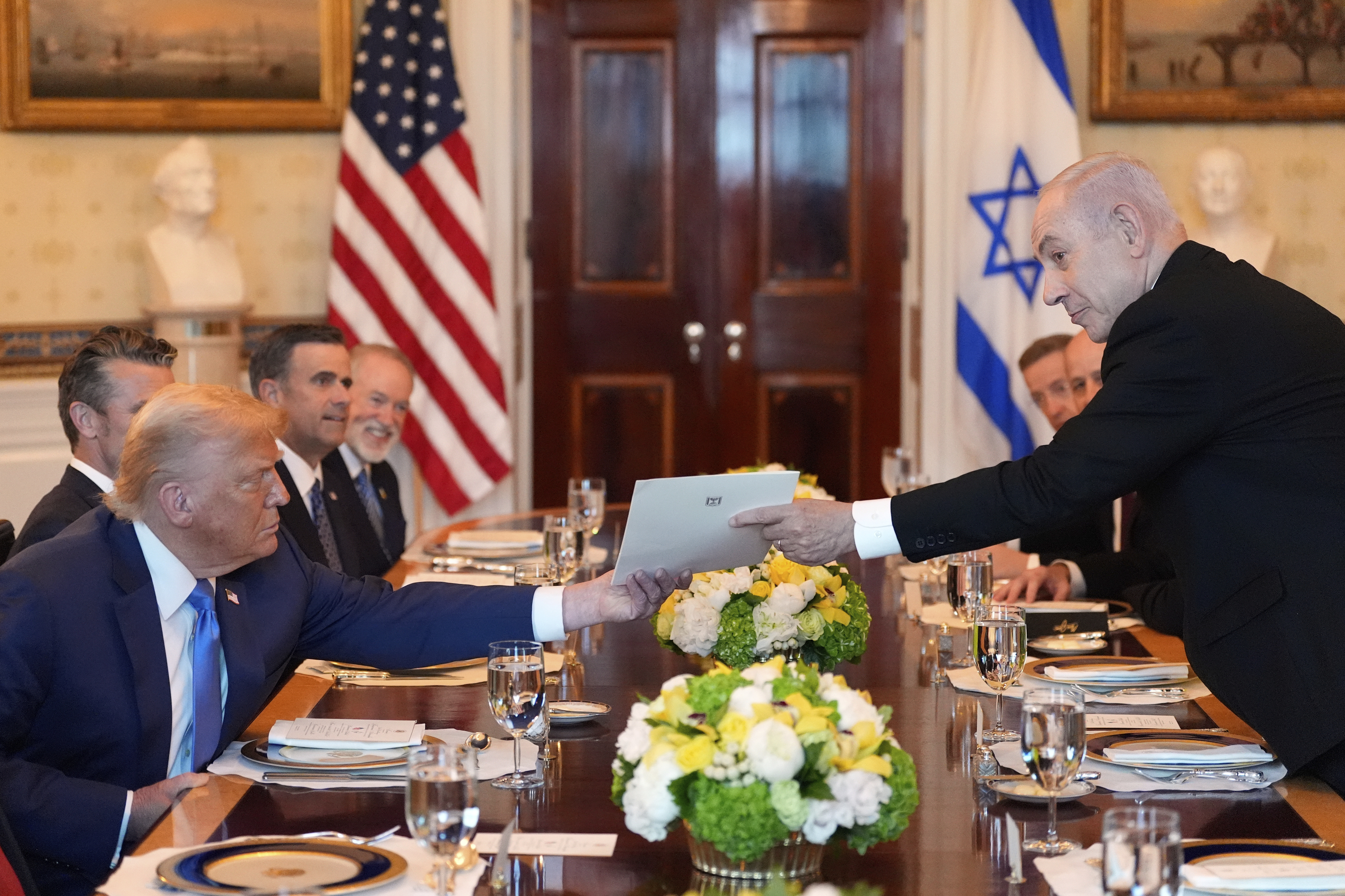 Benjamin Netanyahu hands Trump a document from across a table.