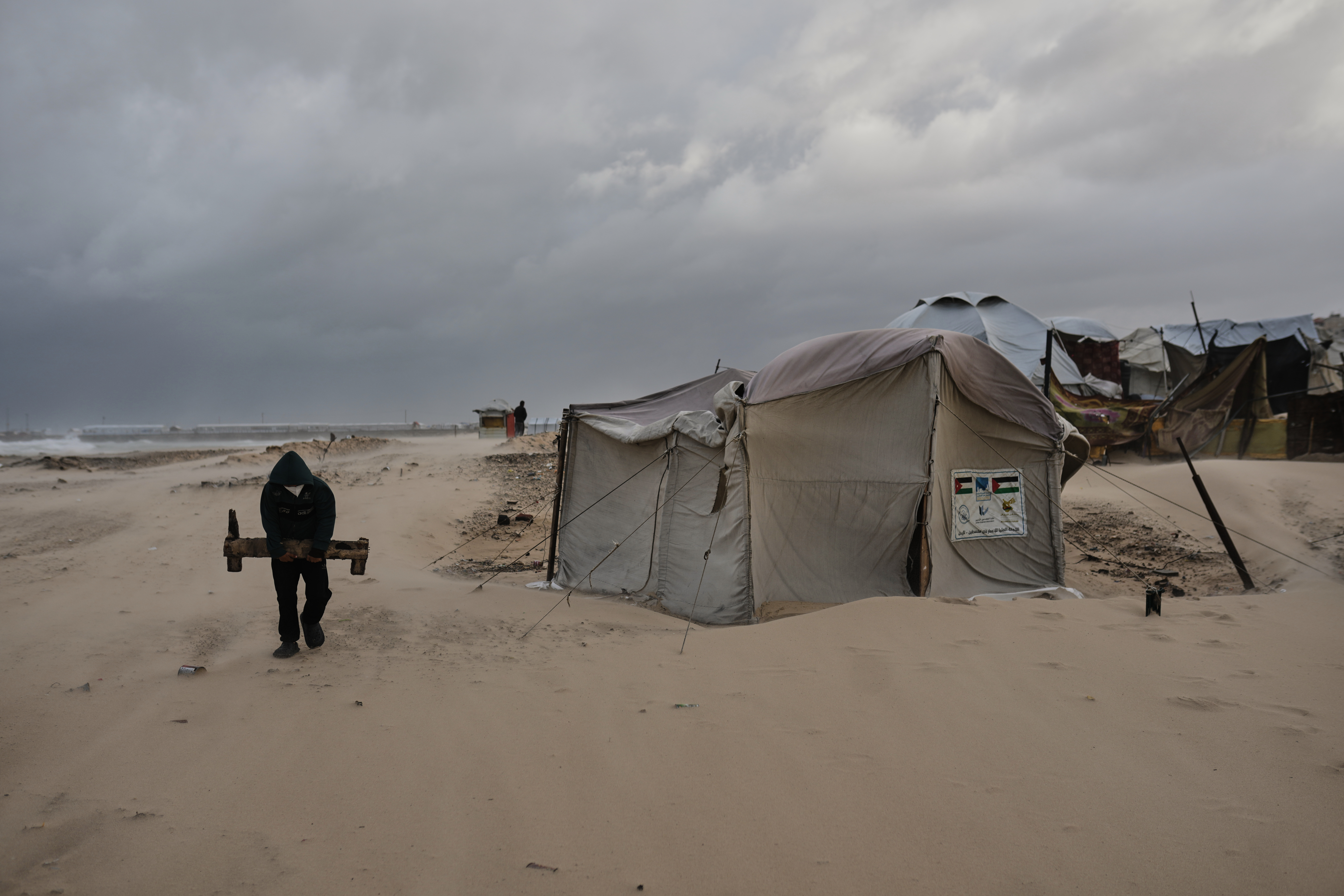 A man carries a piece of wood at a displacement camp sheltering Palestinians on a beach amid stormy weather in Gaza City