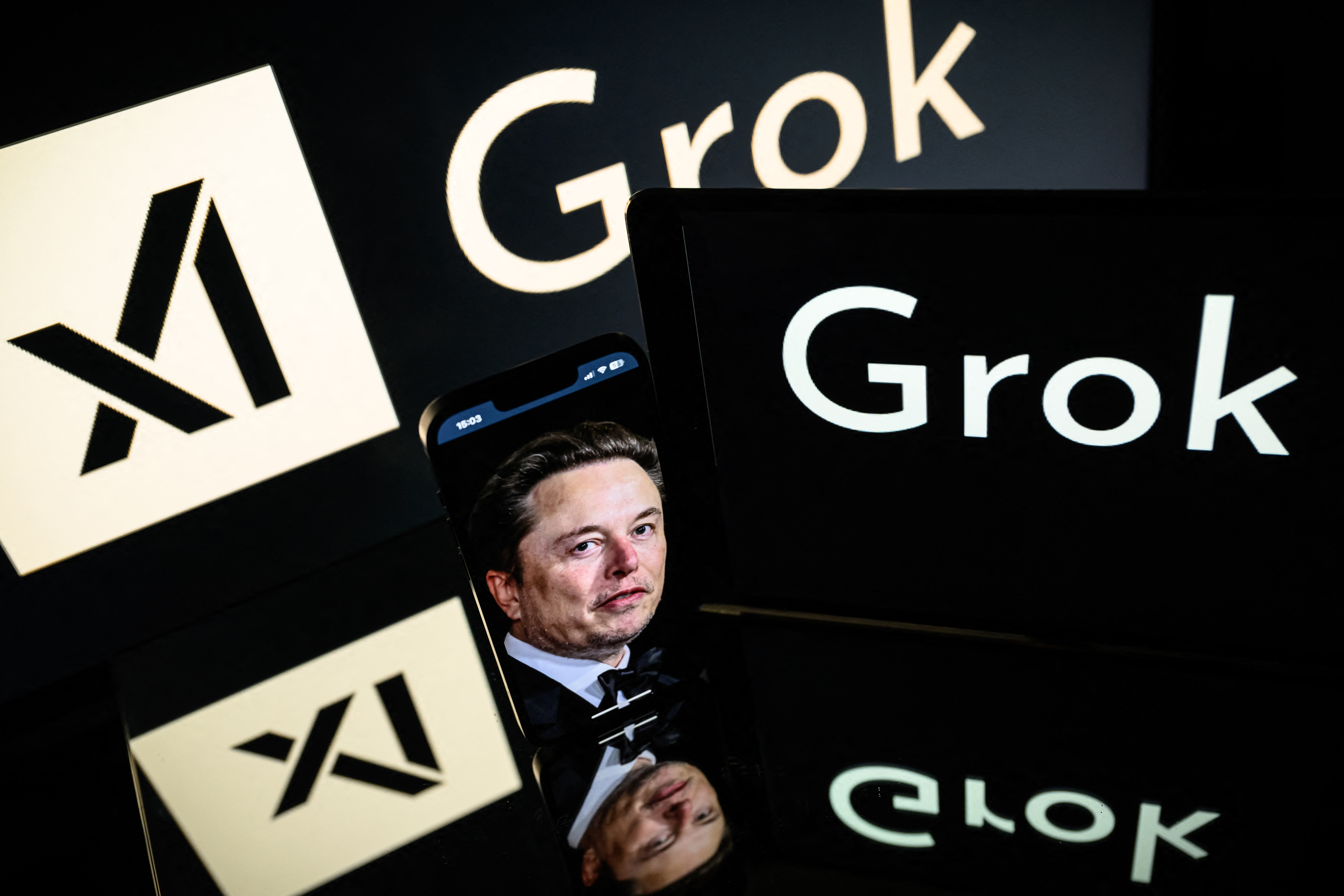 (FILES) This photograph taken on January 13, 2025 in Toulouse shows screens displaying the logo of Grok, a generative artificial intelligence chatbot developed by xAI, the American company specializing in artificial intelligence and it's founder South African businessman Elon Musk.