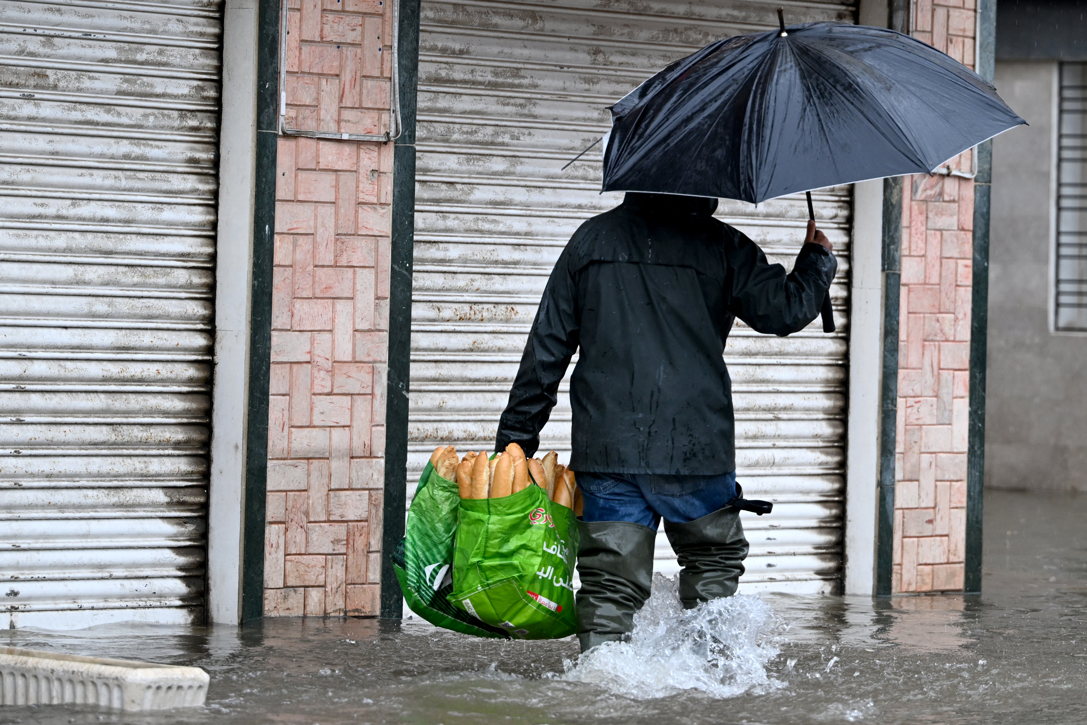 A man carries a bag of bread as he wades through flood waters, in La Goulette near the capital Tunis, on Januray 20, 2026.