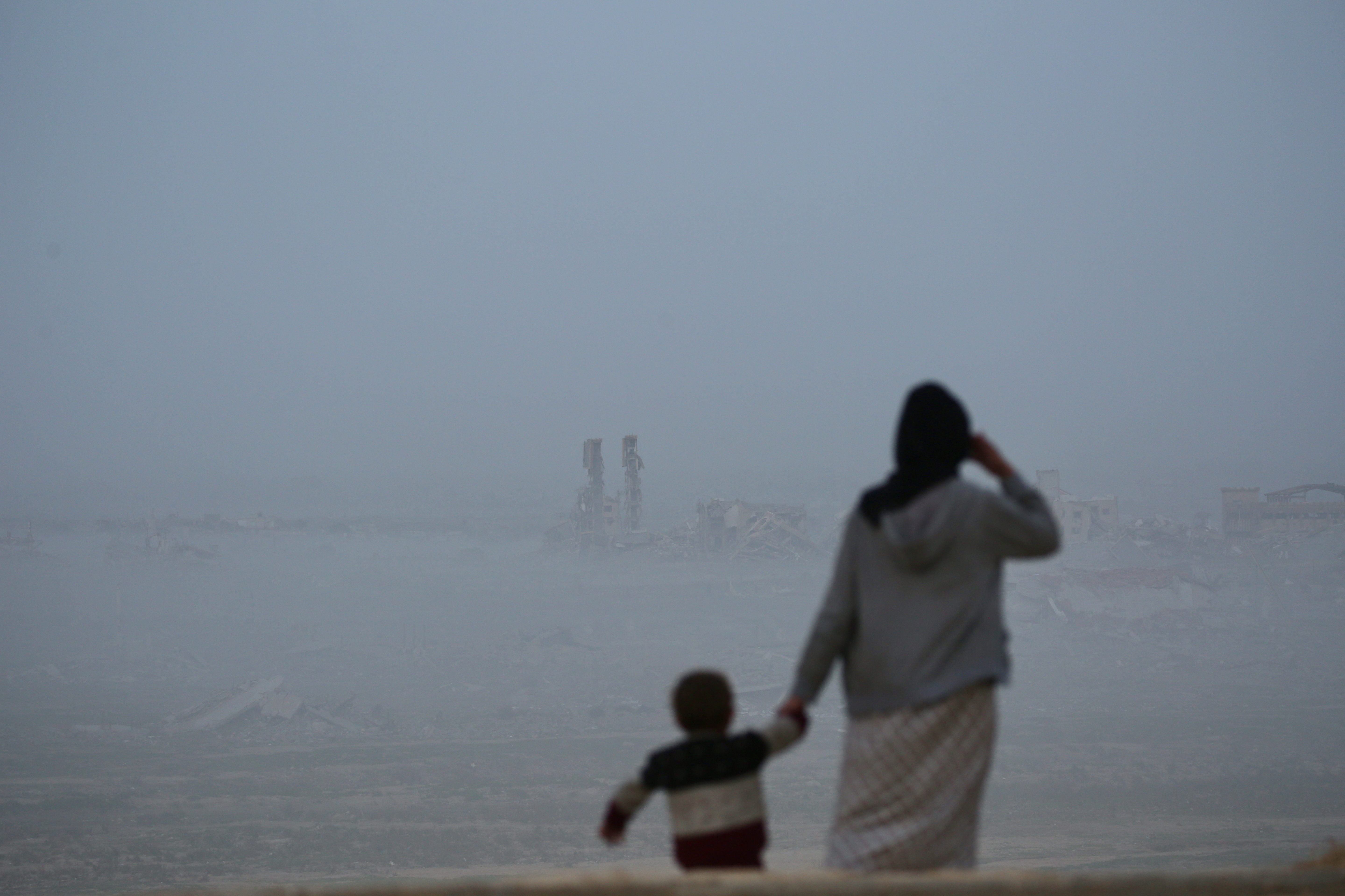 A woman holding a young boy looks towards destroyed buildings at Nuseirat camp for Palestinian refugees in the central Gaza Strip on January 31, 2026.