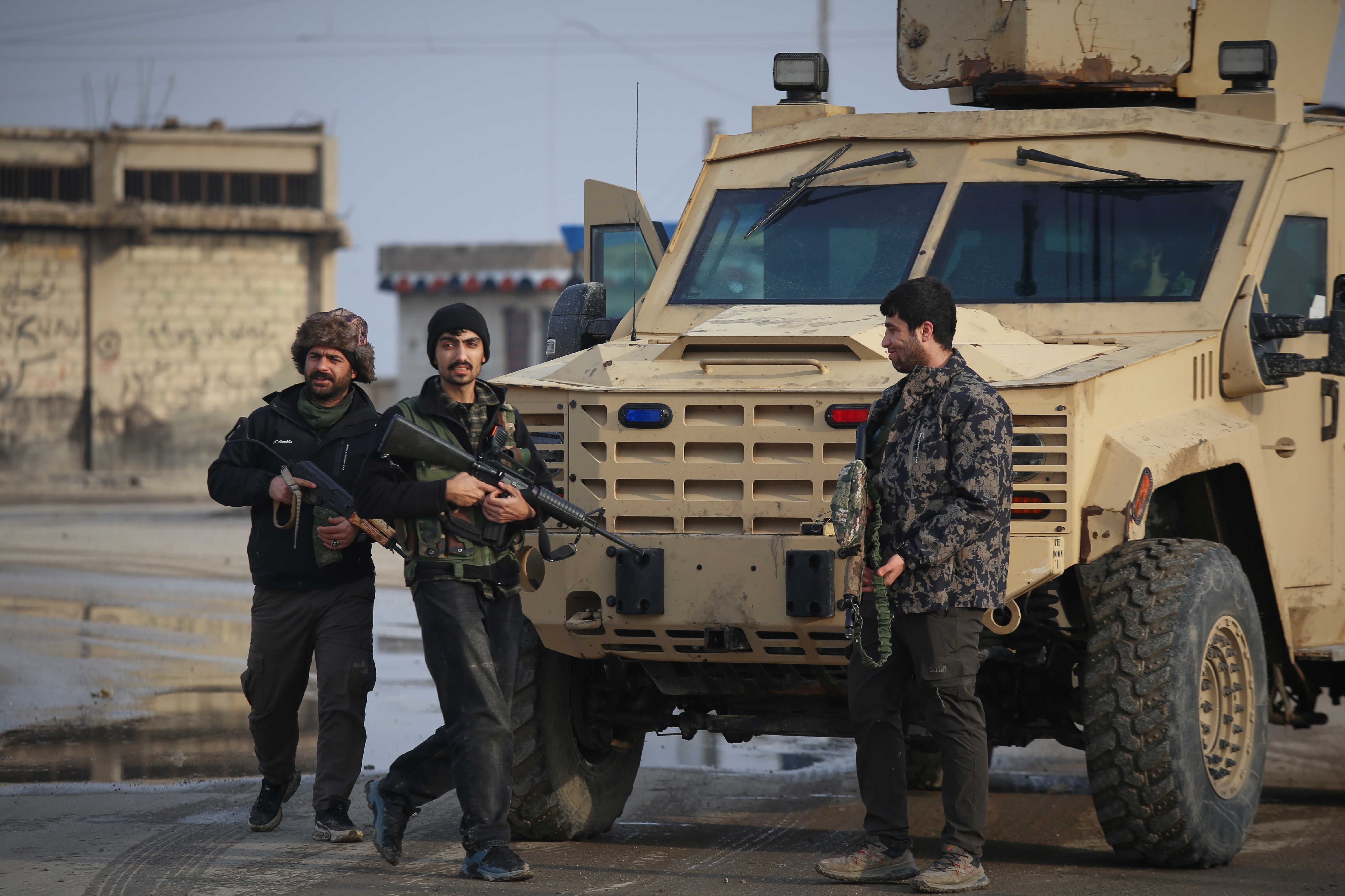 Armed fighters stand in front of a military vehicle.