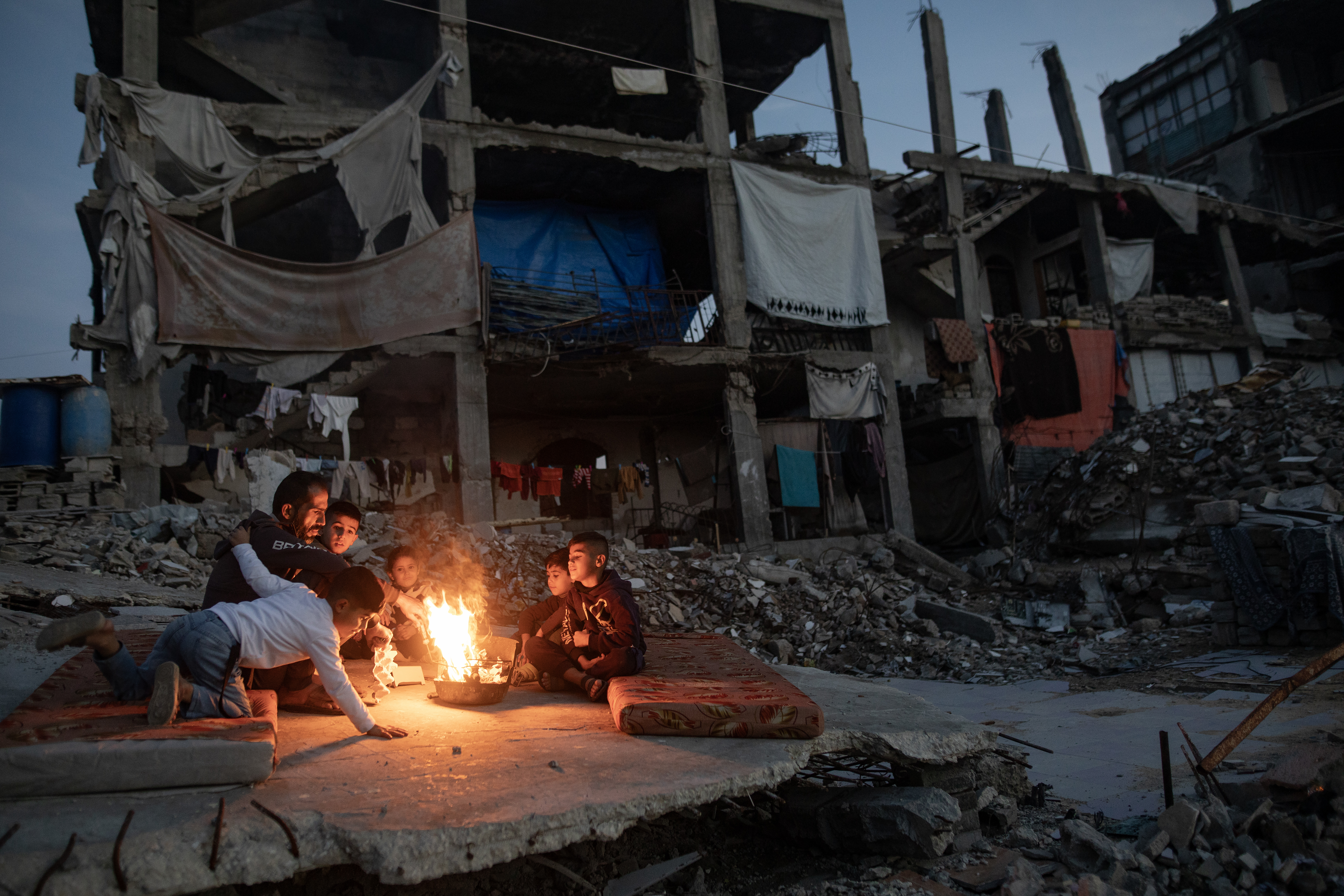epa12618098 Displaced Palestinians warm themselves near a fire among the ruins of their destroyed home in Khan Yunis, southern Gaza Strip, 30 December 2025, amid a ceasefire between Israel and Hamas. EPA/HAITHAM IMAD