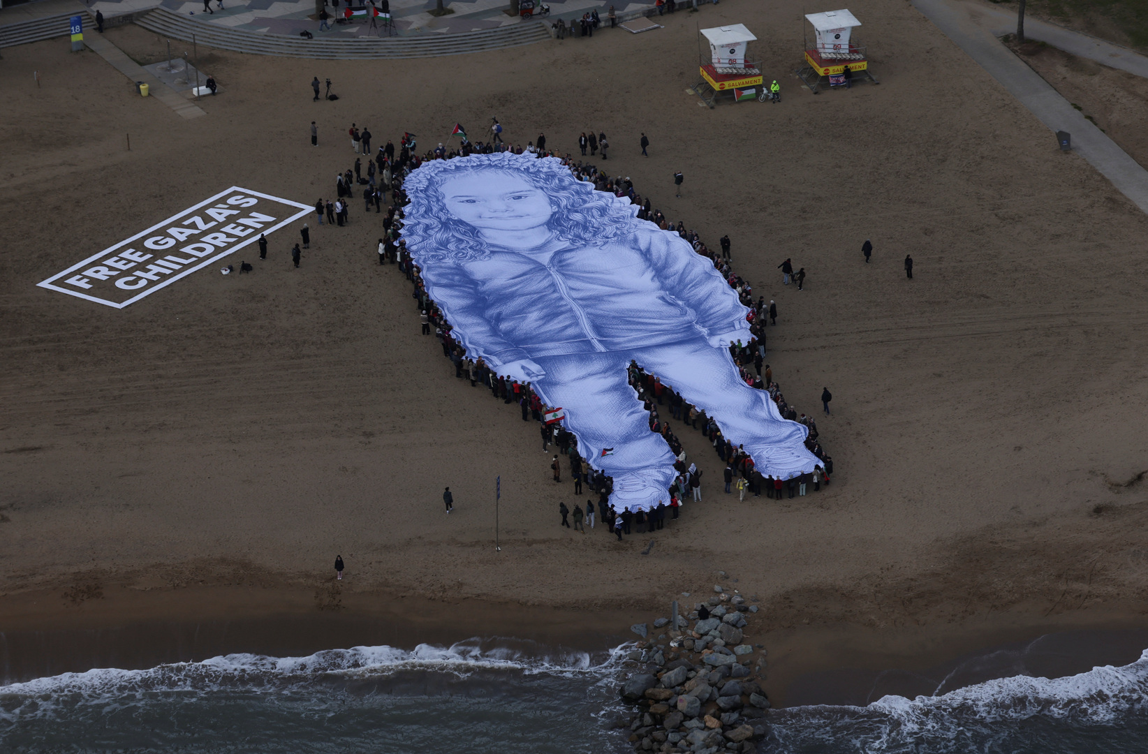 A giant portrait of 5-year-old Palestinian girl Hind Rajab who was killed in Gaza in 2024, is unfurled on Barceloneta Beach in the second anniversary of her death and after a film about her death received an Oscar nomination, in Barcelona, Spain on Jan. 29, 2026. [Nacho Doce/Reuters]
