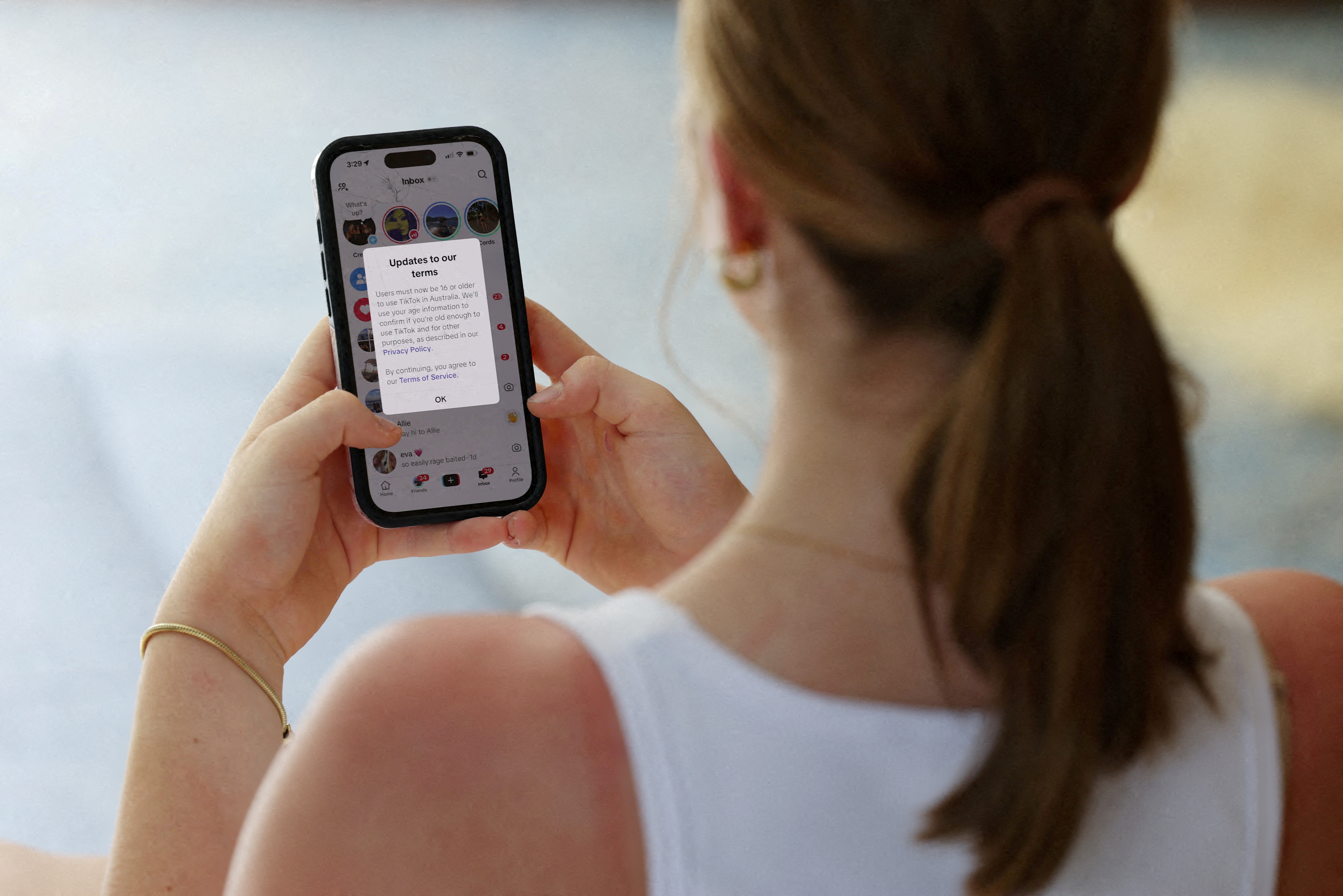 A teenager poses holding a mobile phone displaying a message from TikTok as law banning social media for users under 16 in Australia takes effect, in Sydney, Australia, December 10, 2025 [File: Hollie Adams/Reuters]
