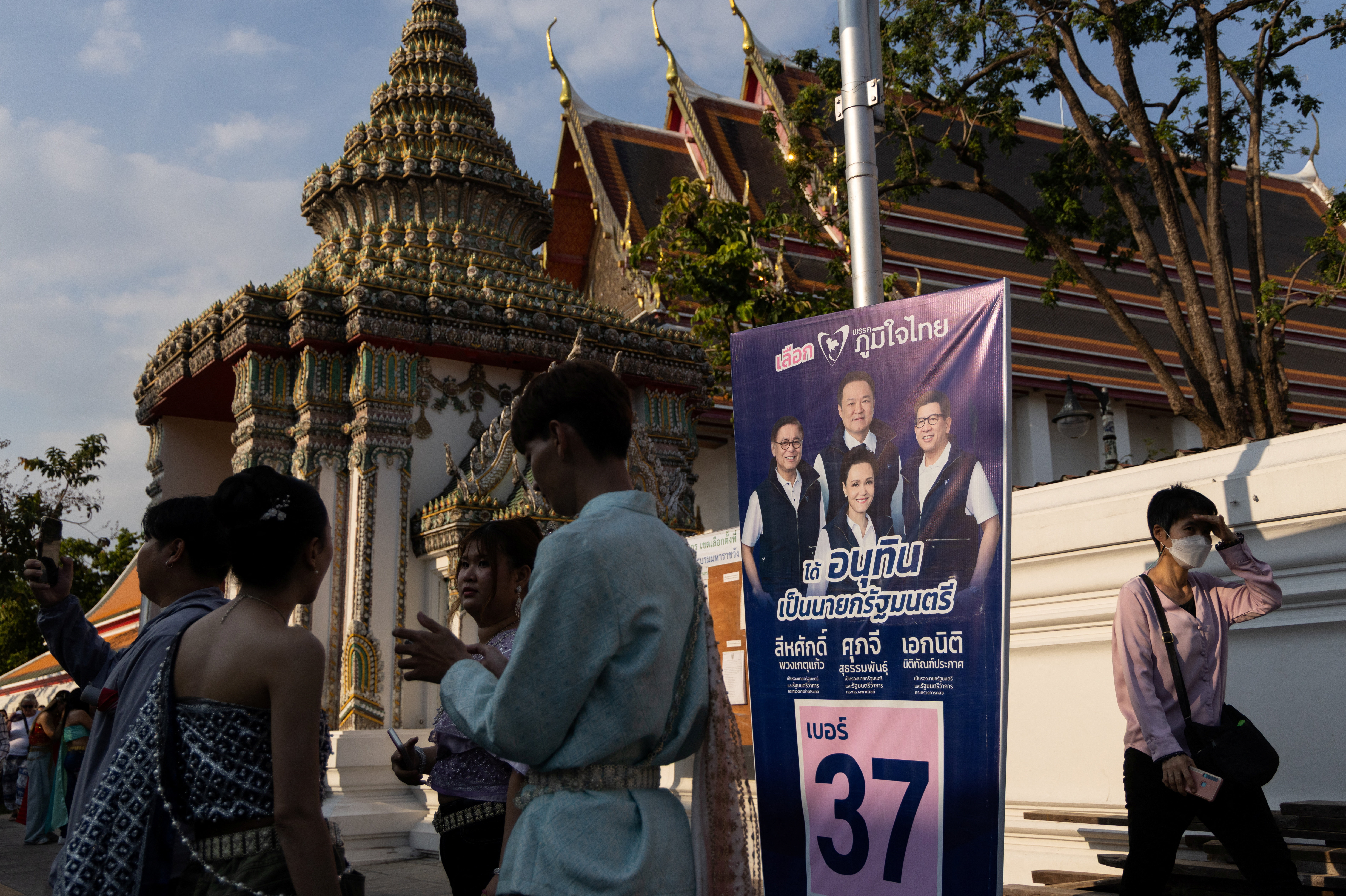 People wearing traditional Thai dress gather next to a campaign poster of Bhumjaithai party in the tourist district, as Thailand will hold general elections on February 8, in Bangkok, Thailand, February 7, 2026. REUTERS/Maxim Shemetov