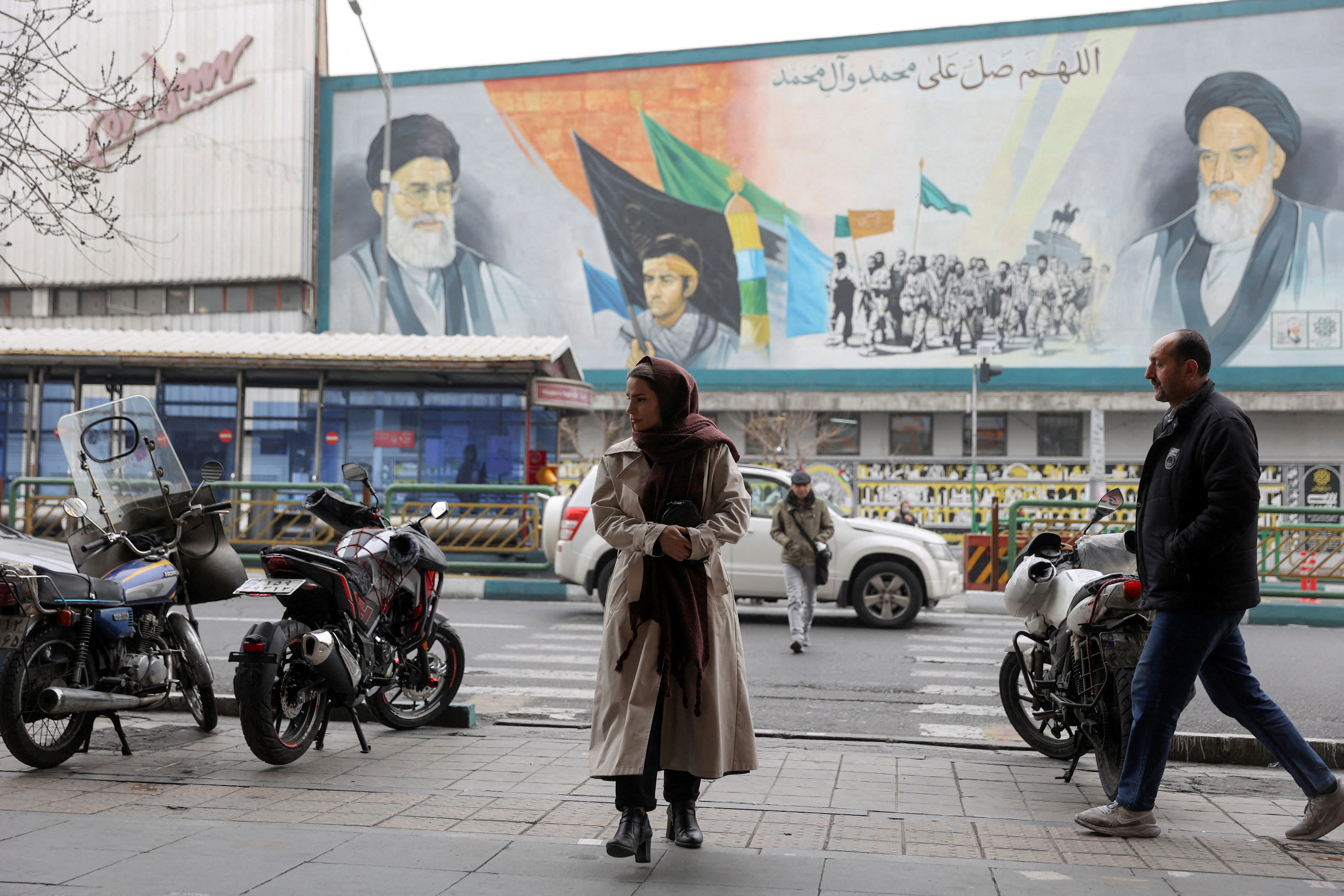 People walk next to a mural with a picture of Iran's Supreme Leader, Ayatollah Ali Khamenei, on a street in Tehran
