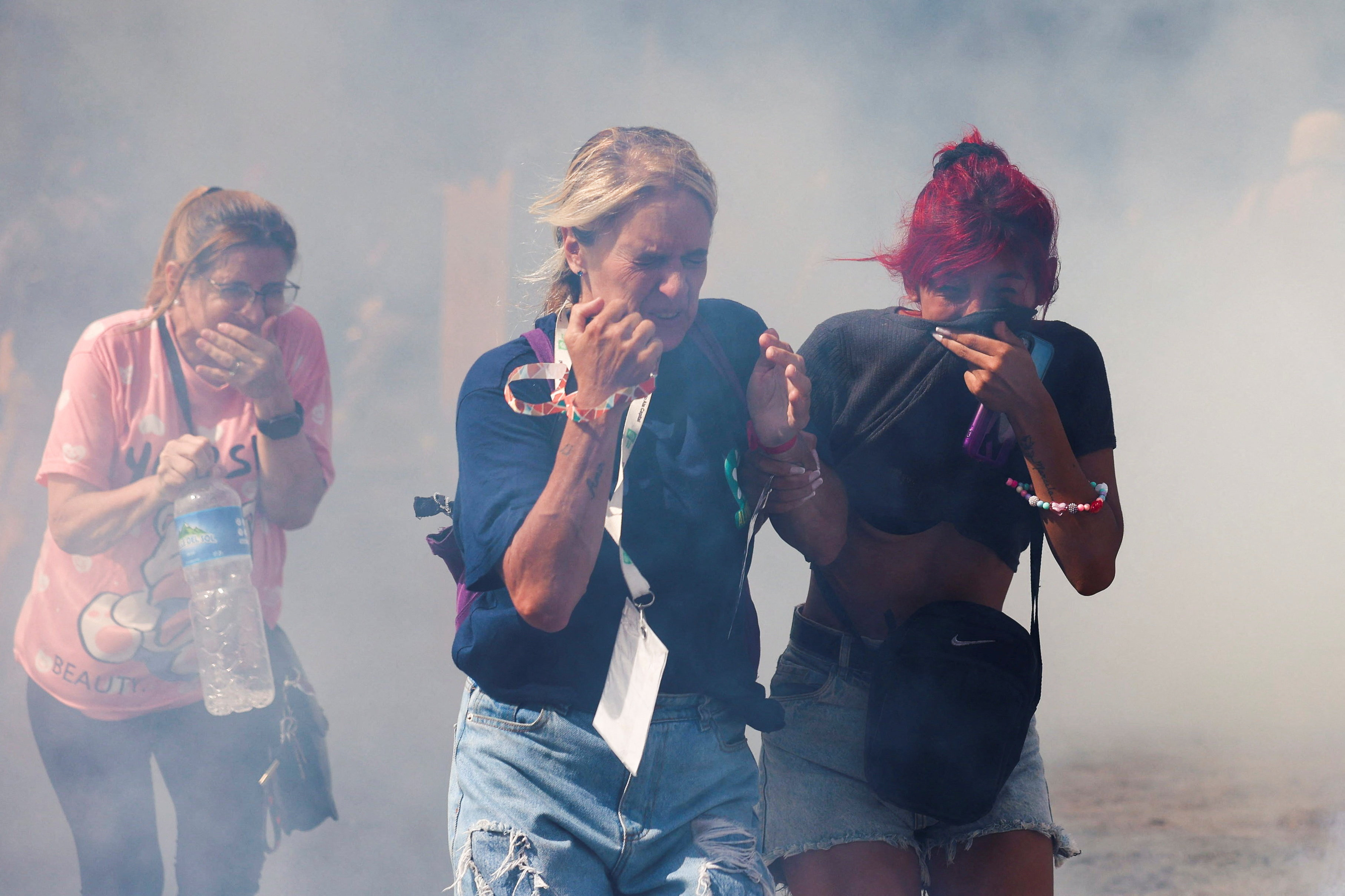 women try to cover their faces as they walk through a cloud of tear gas during a labour demonstration