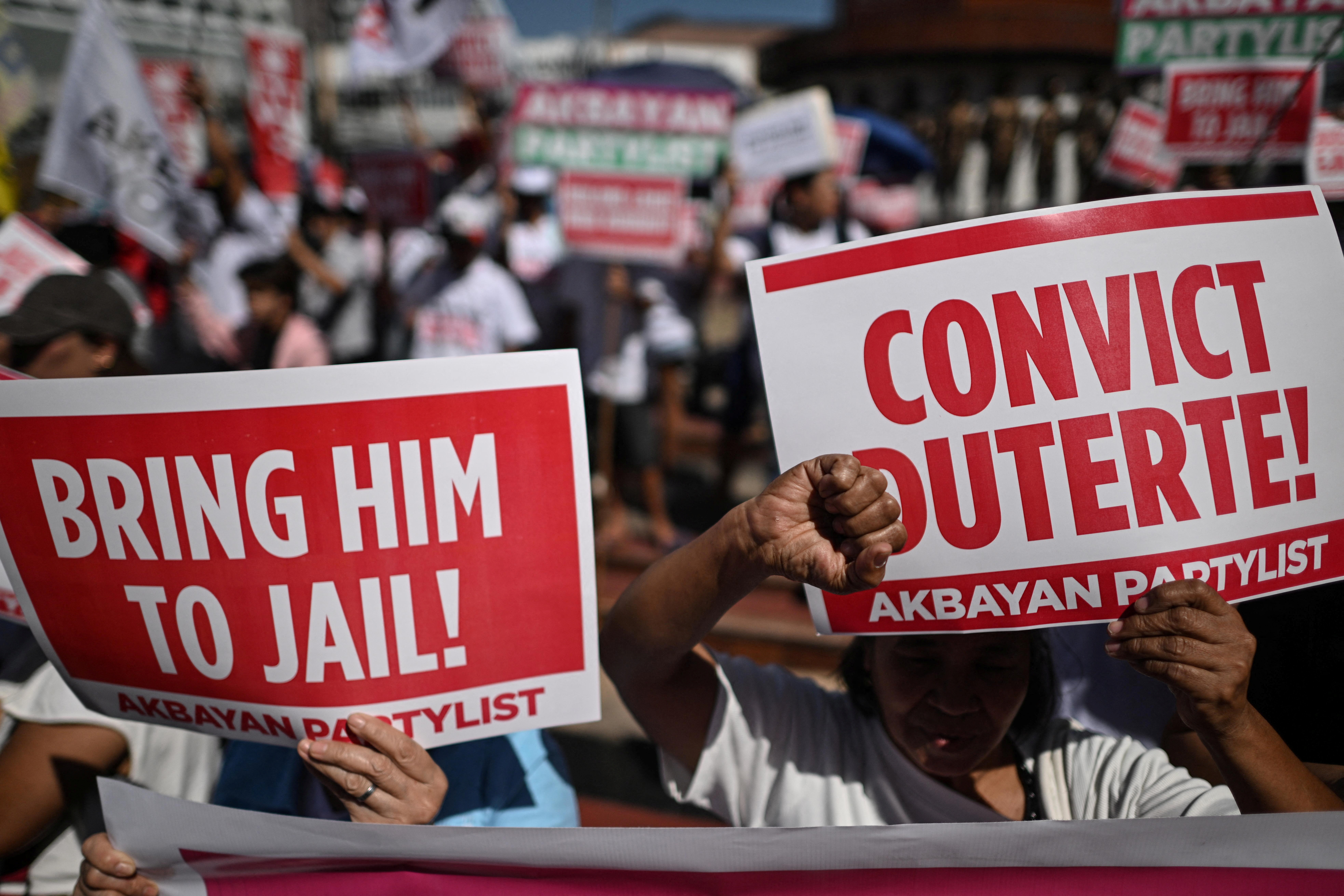 Protesters hold placards during a rally before former Philippine President Rodrigo Duterte's pre-trial hearings