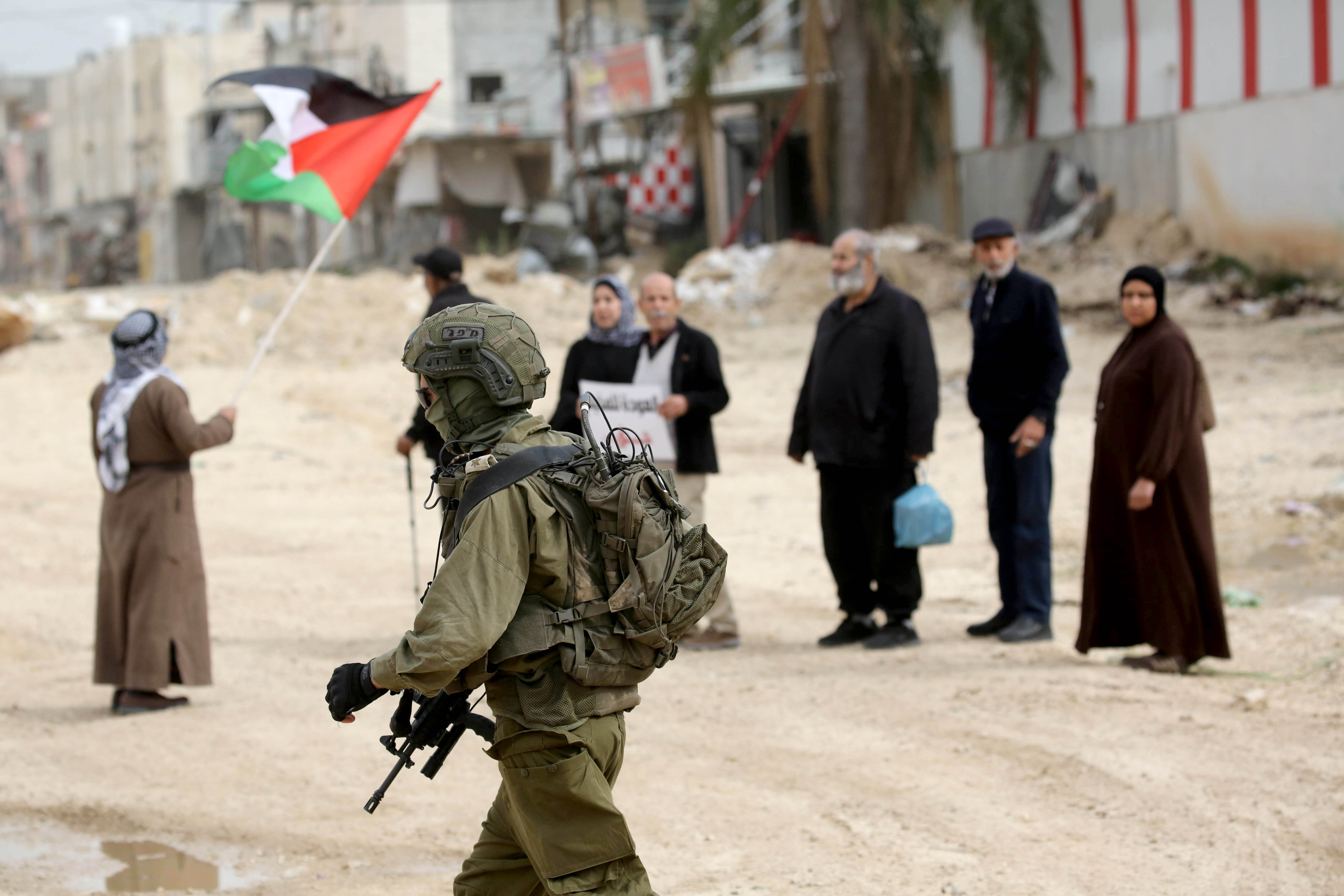 Israeli army soldier stands in front of Palestinians