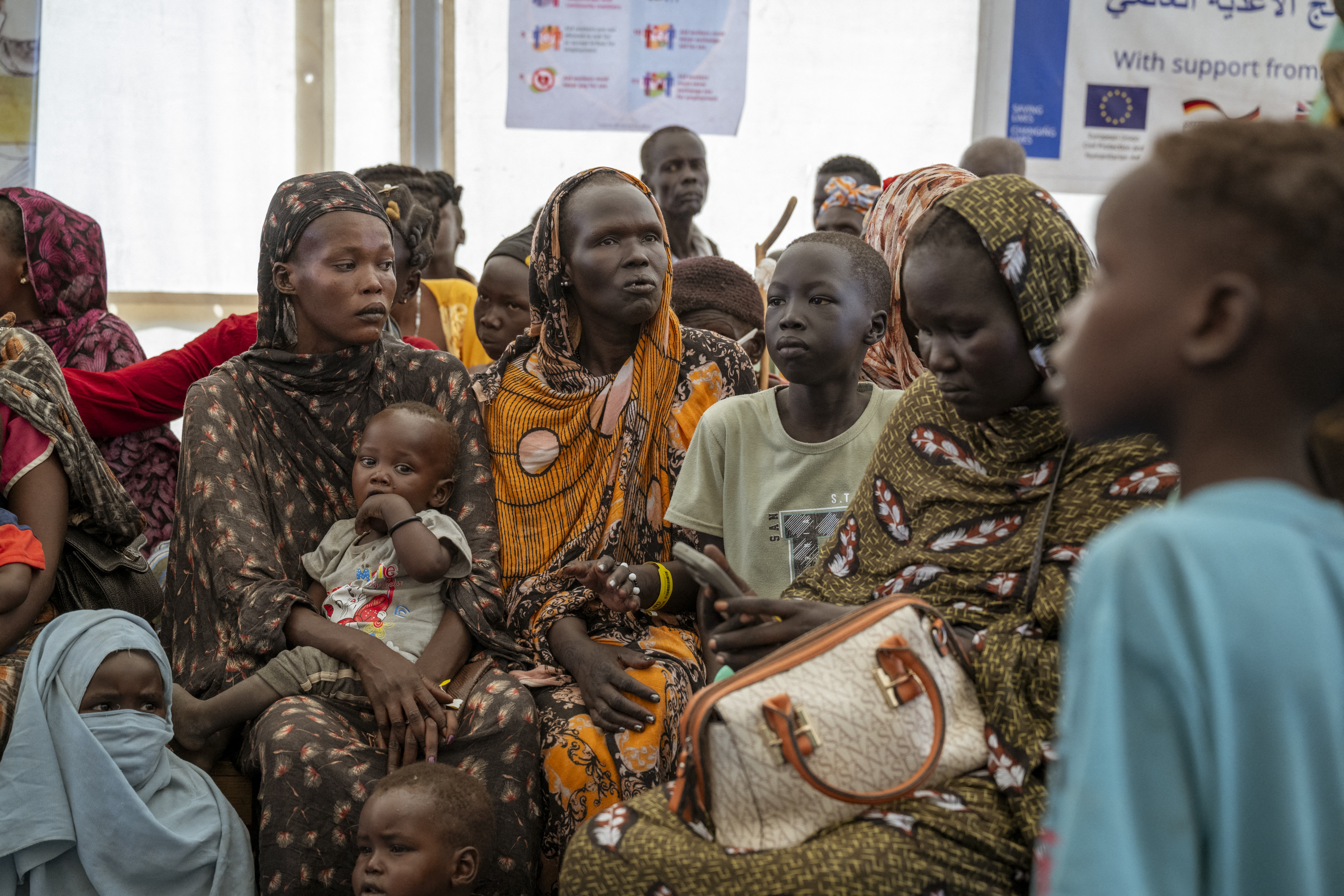 A group of women and young children wait for aid.