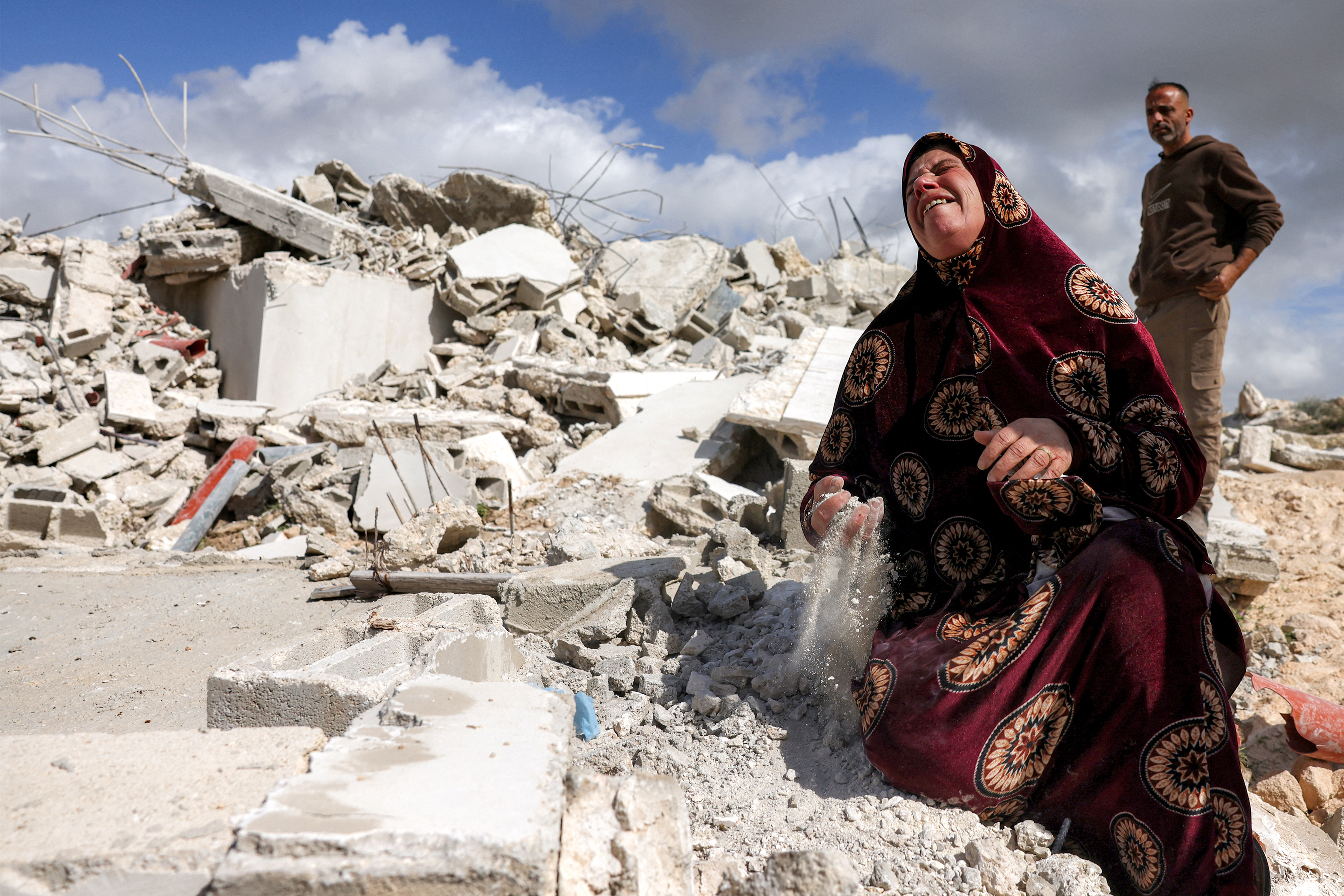 A Palestinian woman reacts as she holds the dust from the rubble of her house which was demolished by Israeli security forces, in the Palestinian village of Beit Awa in the southwest of the occupied West Bank on February 11, 2026. [HAZEM BADER / AFP]