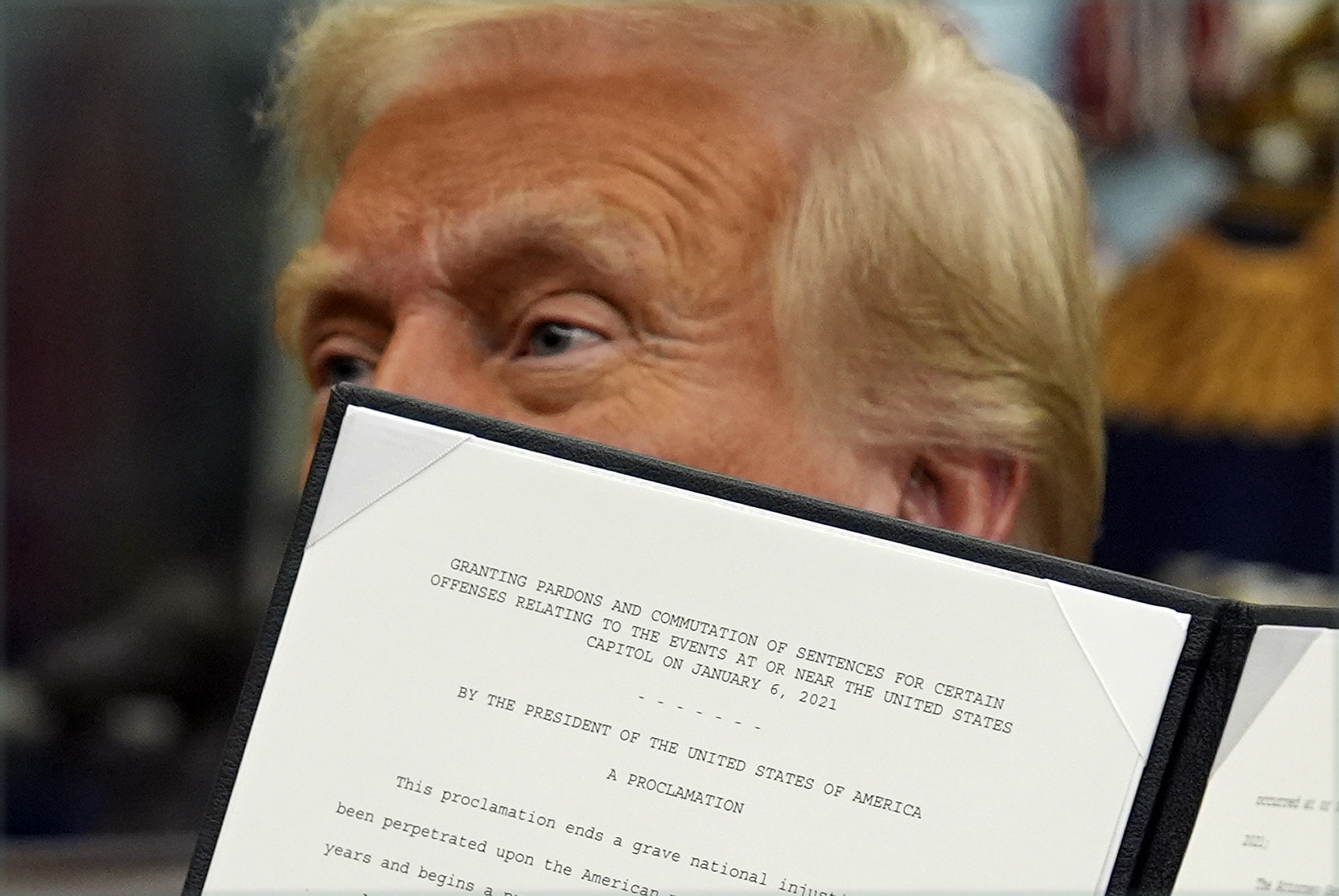Donald Trump holds up an executive order pardoning January 6 rioters