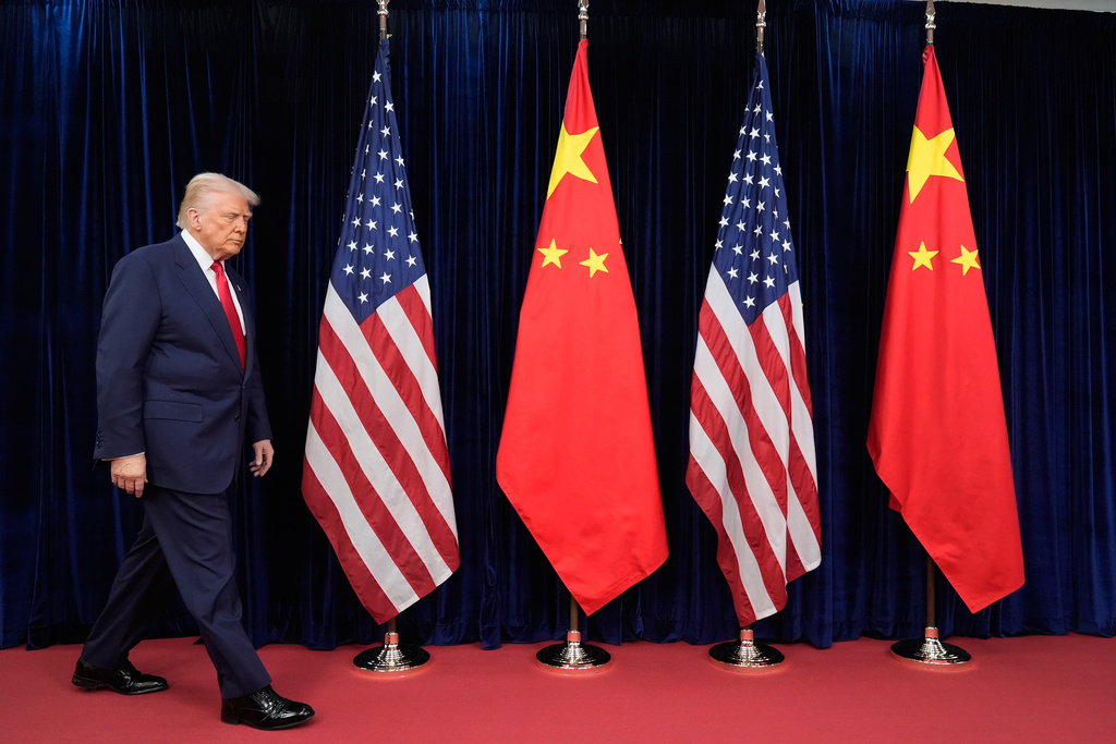 a man in a suit walks in front of US and Chinese flags