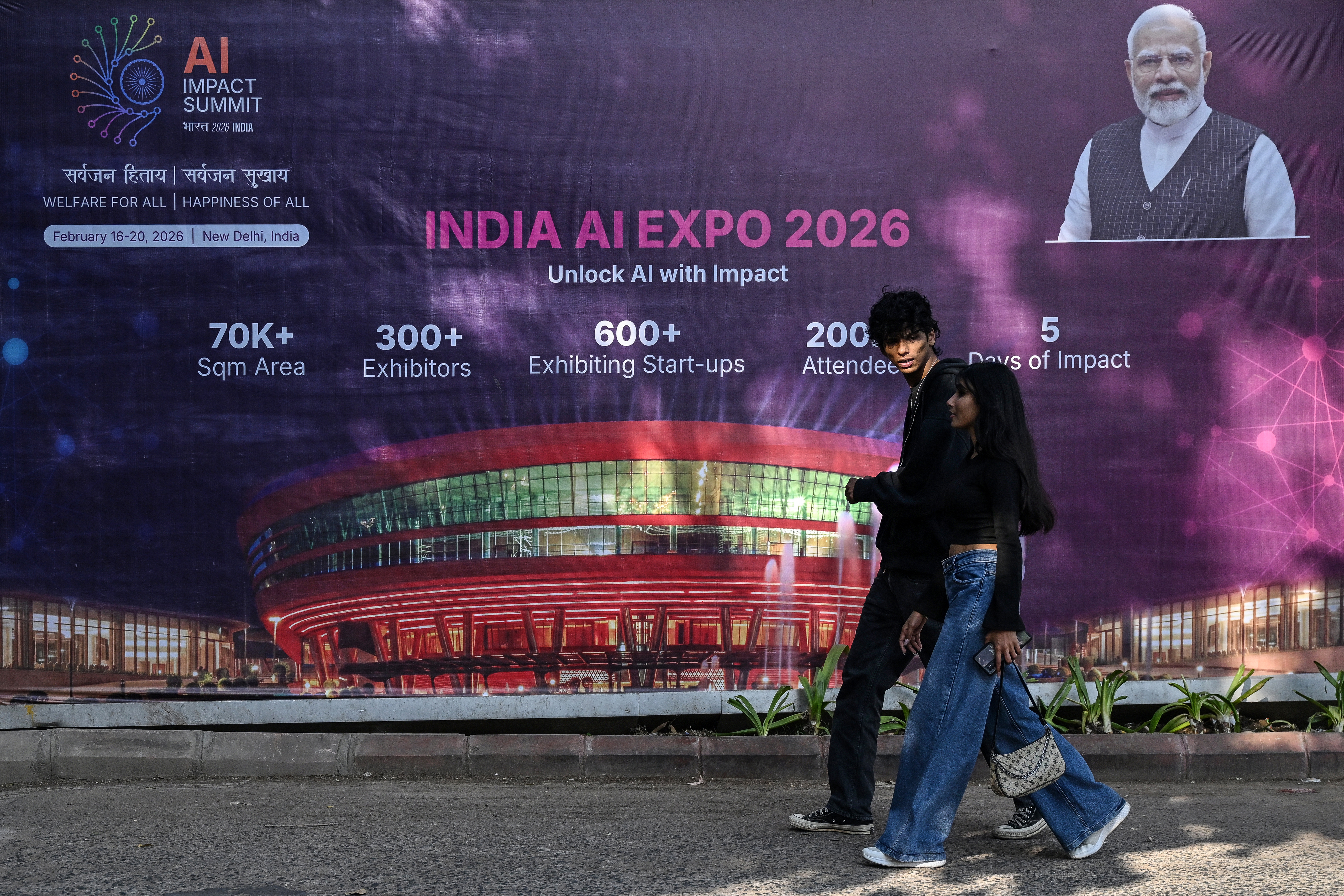 People walk past a hoarding of the AI Expo in New Delhi on February 15, 2026