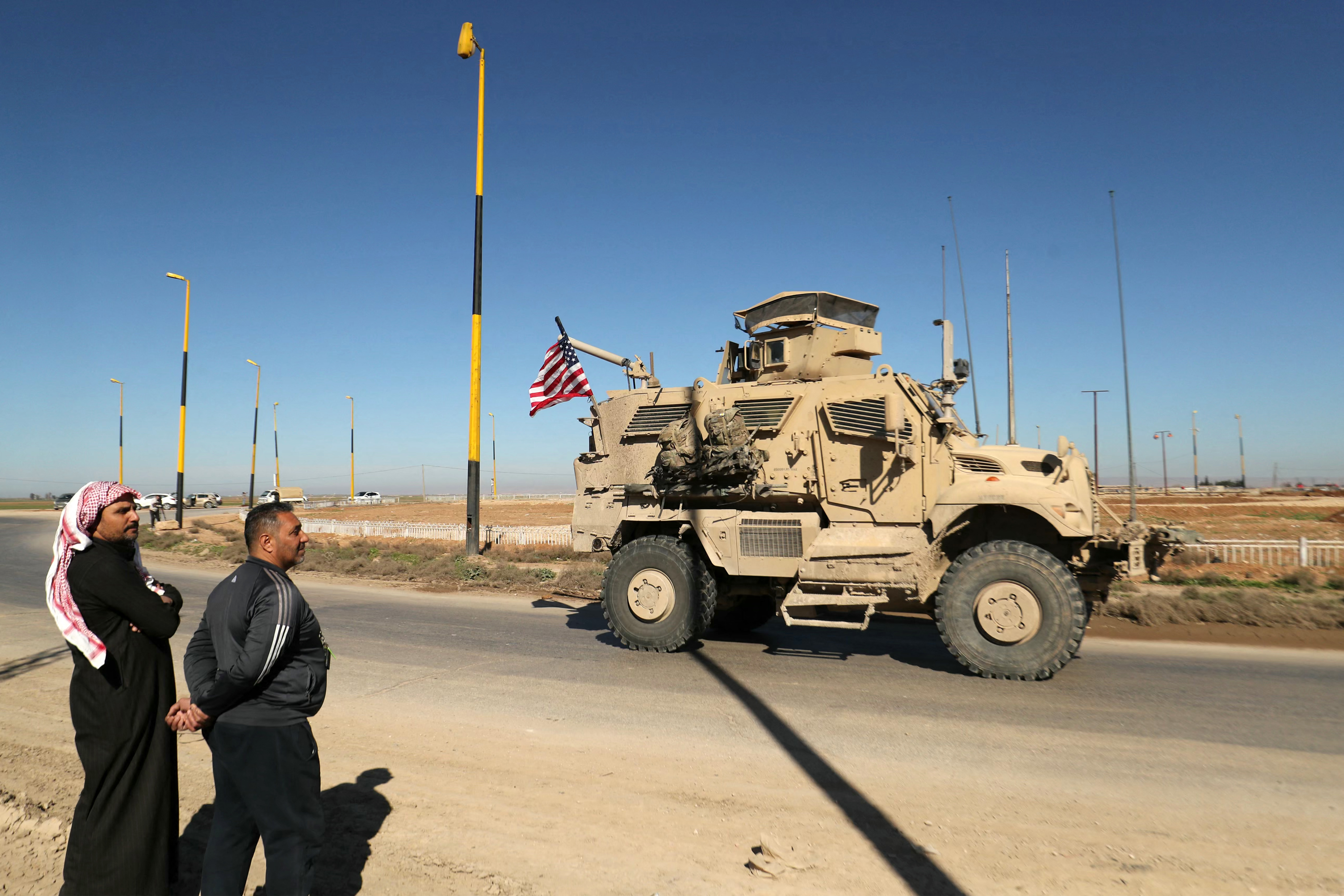 TOPSHOT - Men watch as a US military mine-resistant ambush protected (MRAP) armoured fighting vehicle moves in a convoy along a highway outside Qamishli in Syria's northeastern Hasakah province on February 23, 2026.