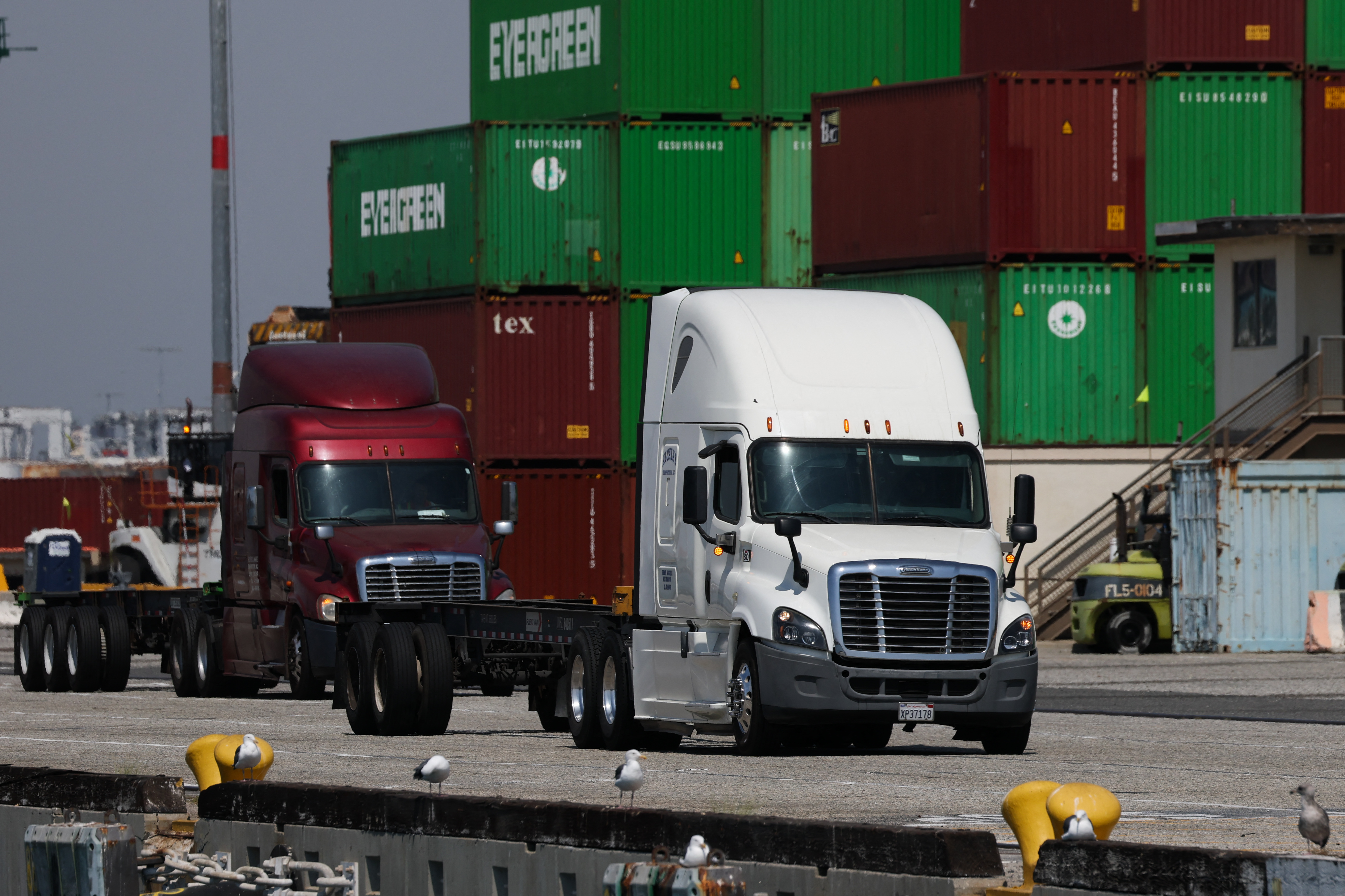 Trucks drive past cargo shipping containers at a shipping terminal.