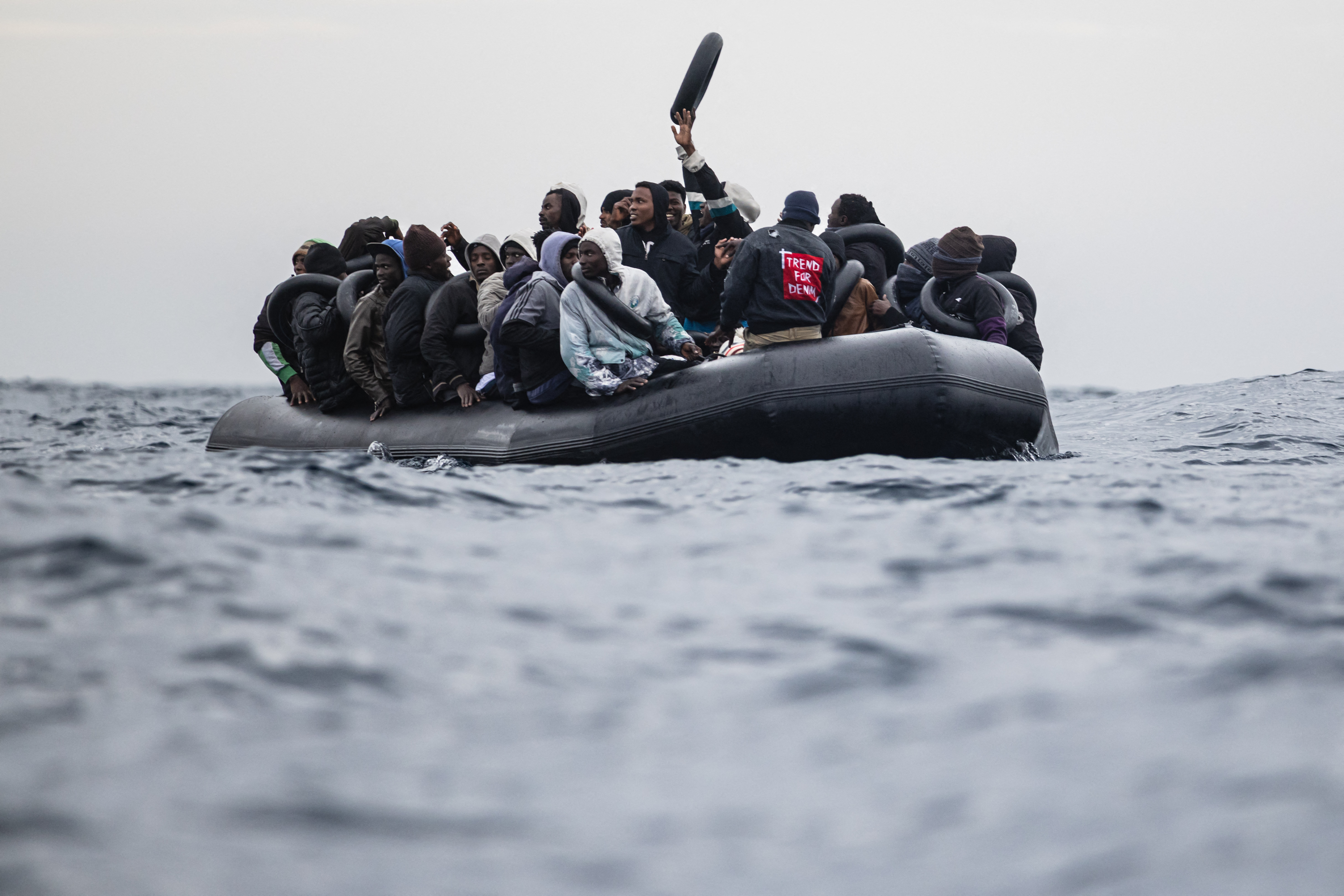 (FILES) Migrants onboard a rubber boat wave and gesture as they wait to be rescued by crew members of the “Ocean Viking” rescue ship in the search-and-rescue zone in the Mediterranean Sea near the Libyan coast, on January 16, 2026.