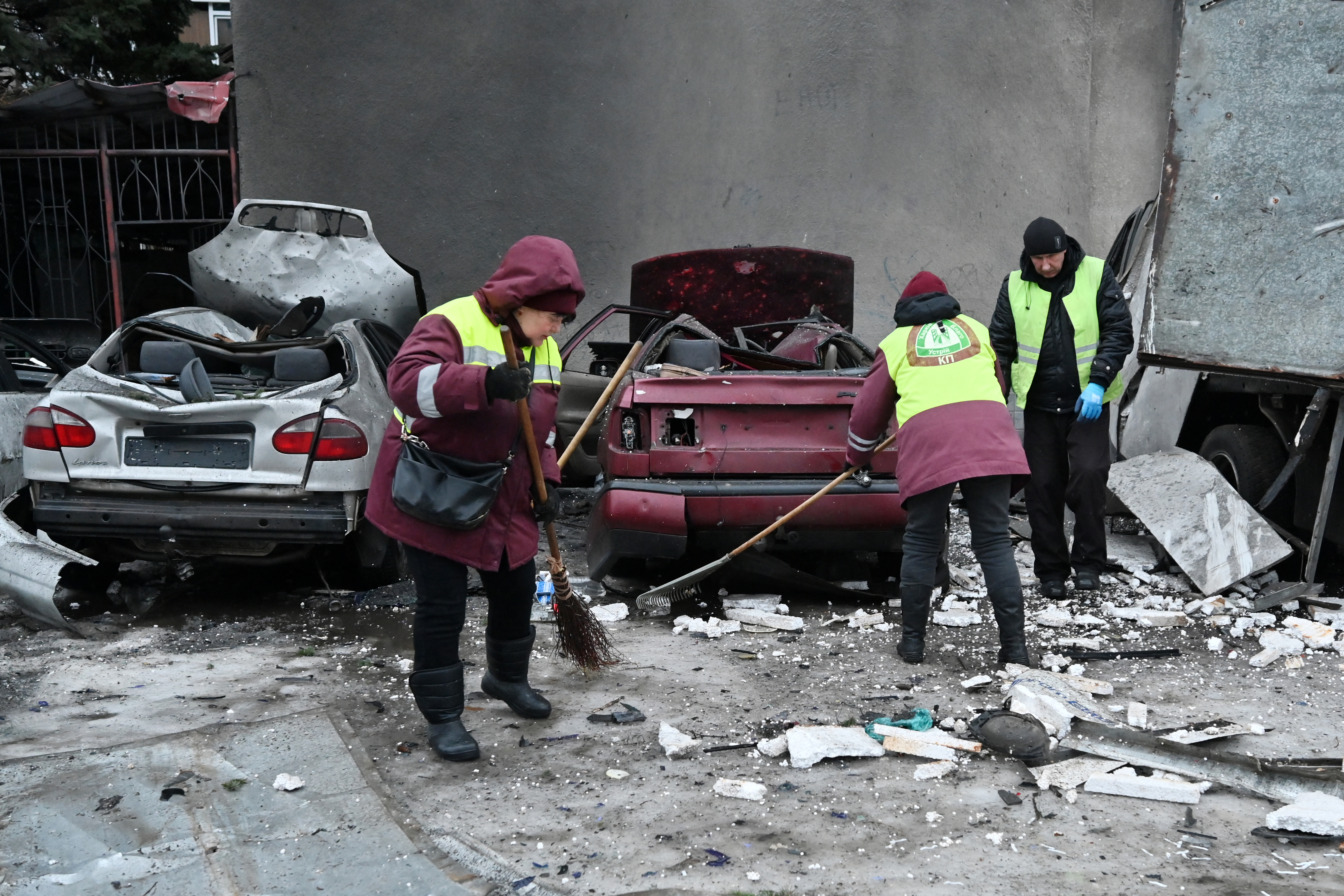 Communal workers clear debris next to destroyed cars in the courtyard of a damaged residential building following an air attack in Kharkiv on February 26, 2026, amid the Russian invasion of Ukraine.