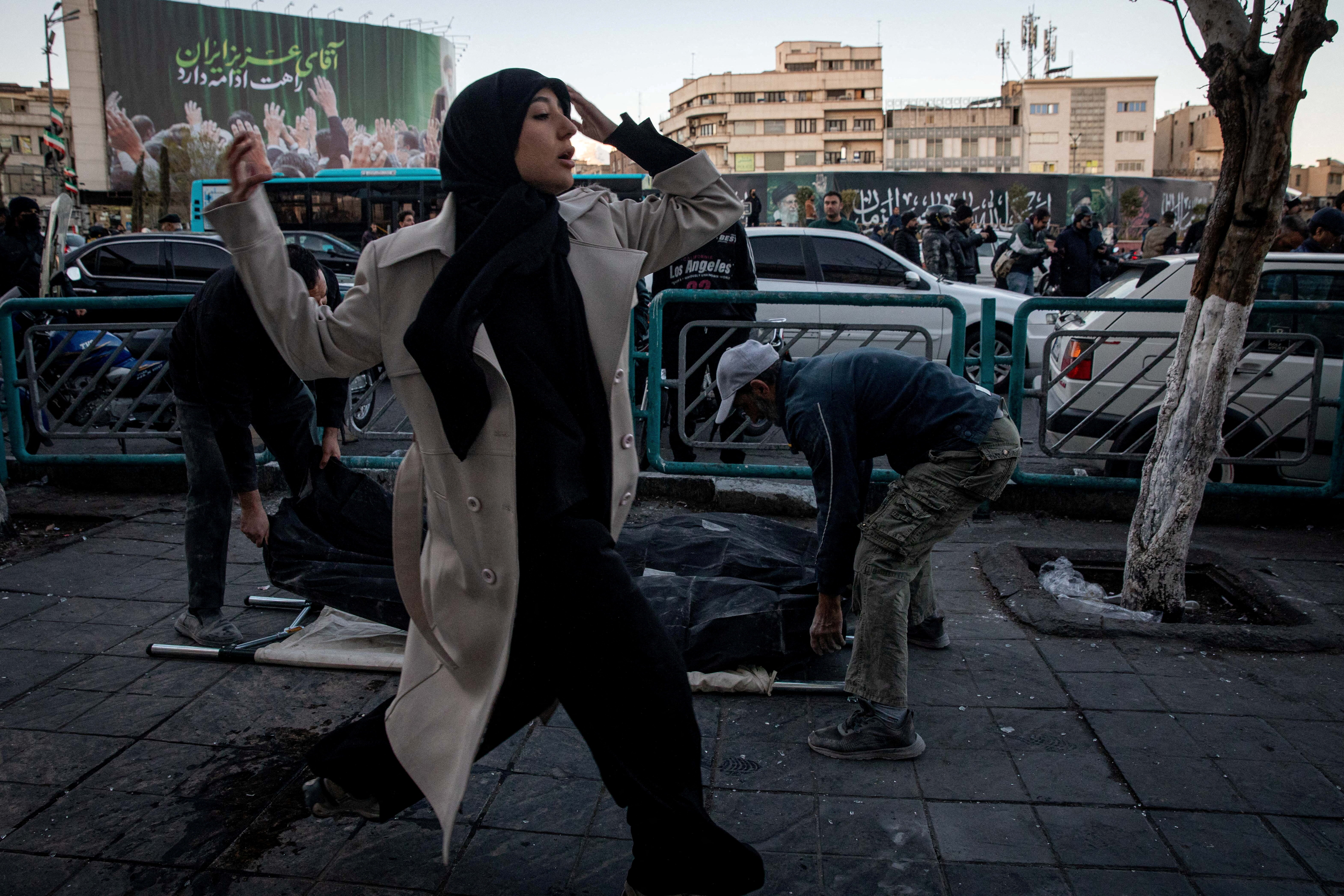 A woman runs past people placing casualties of an Israel and US strike on a police station, on the ground, in Tehran, Iran, March 3, 2026. [Majid Khahi/ISNA/WANA/Reuters]