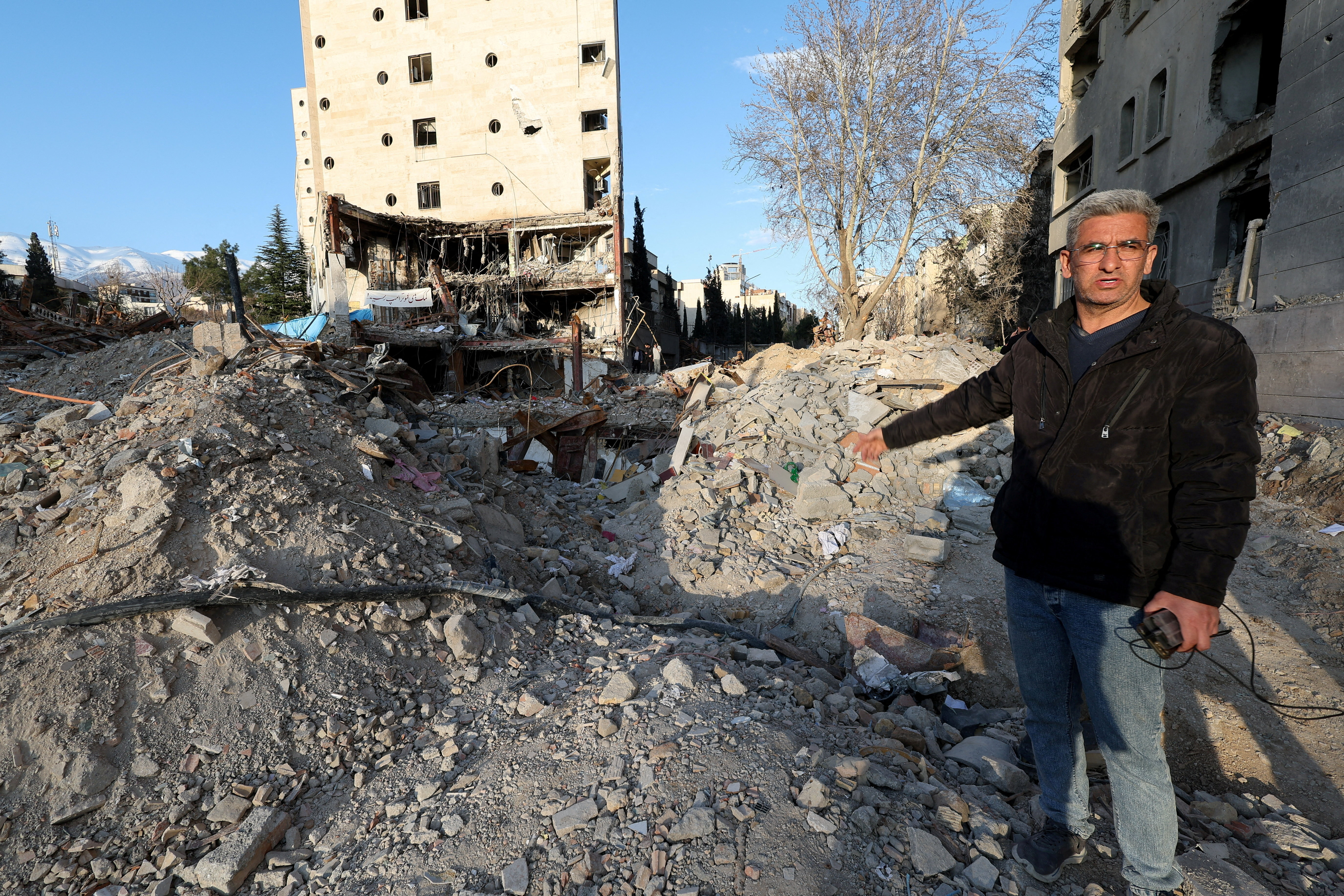 A man gestures at the site of a destroyed building.