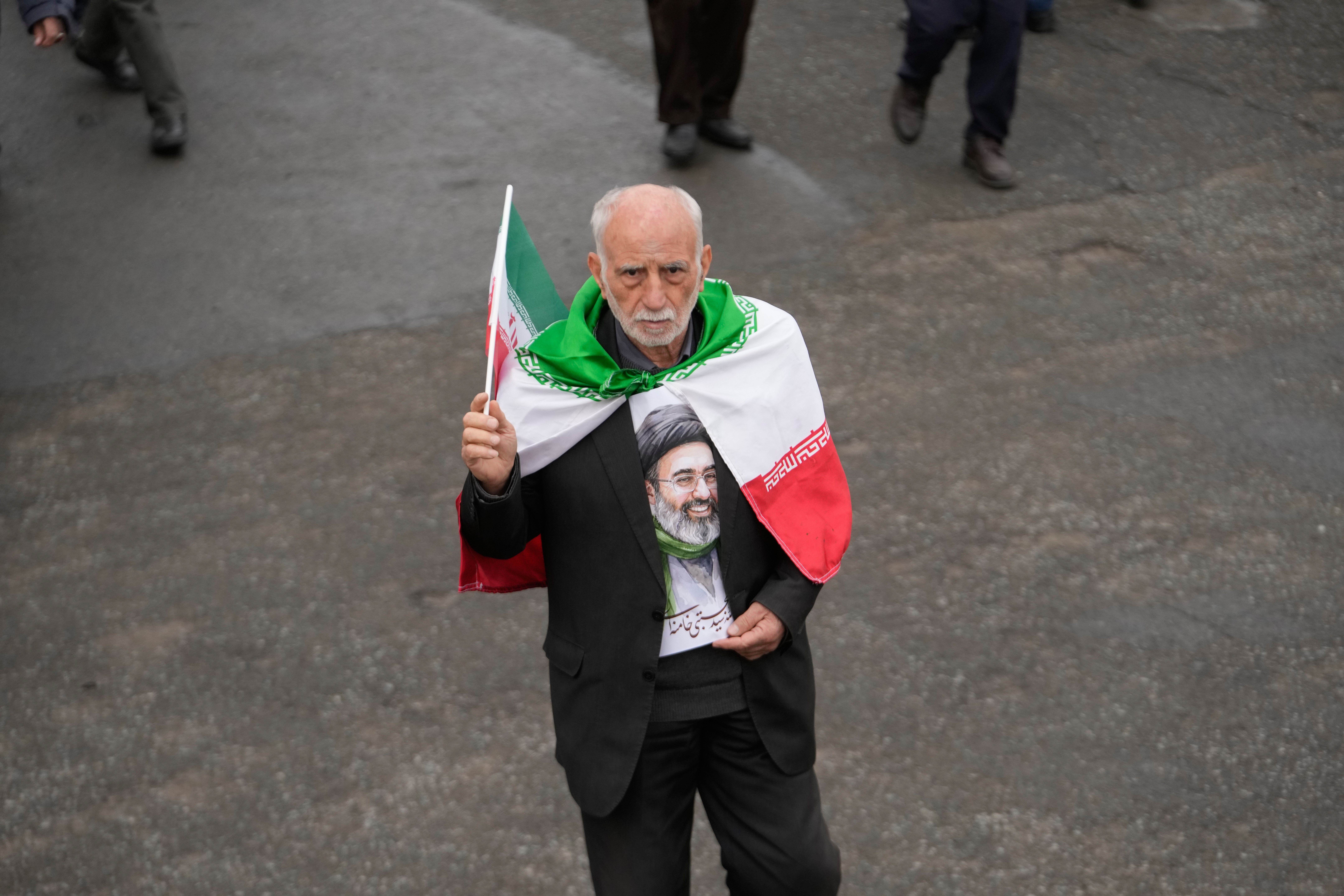 A man wears and holds Iranian flags while holding a poster of the Supreme Leader Ayatollah Mojtaba Khamenei after the conclusion of the Friday prayers at the Imam Khomeini Grand Mosque in Tehran, Iran, Friday, March 20, 2026. [Vahid Salemi/AP Photo]