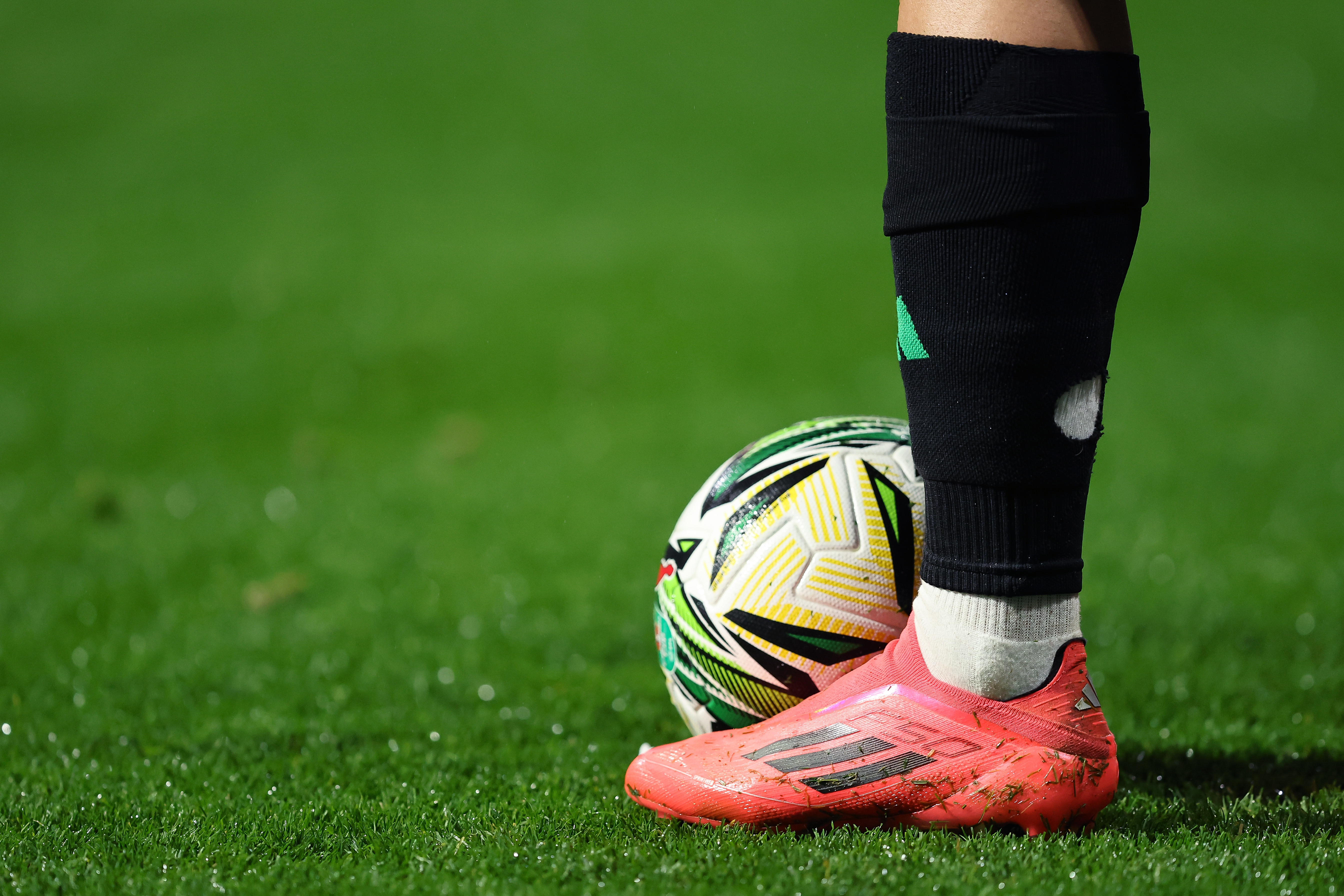 Football player's leg, wearing Addidas shoes, seen next to a football.