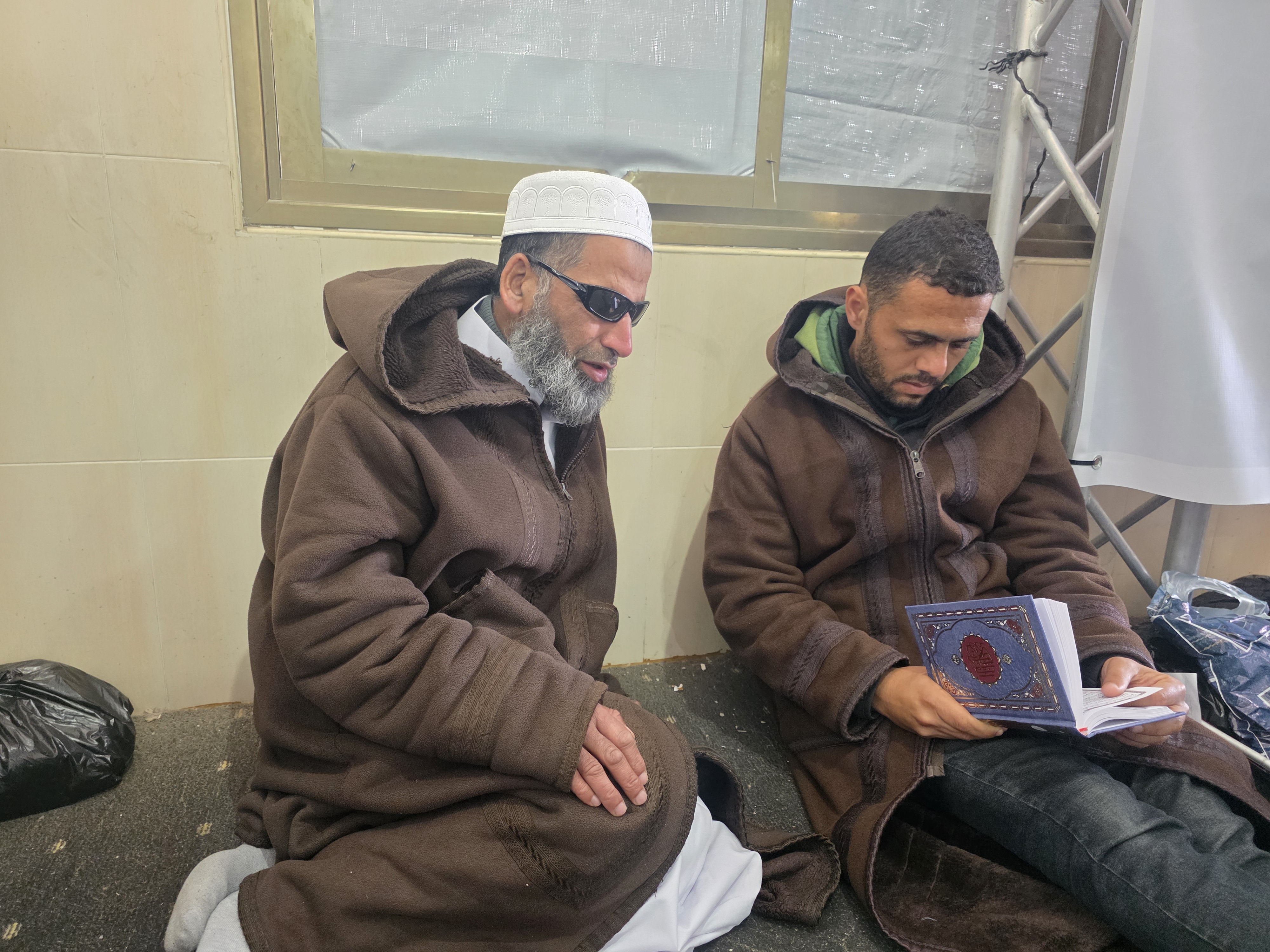A man recites the Quran while another checks his recitation is correct