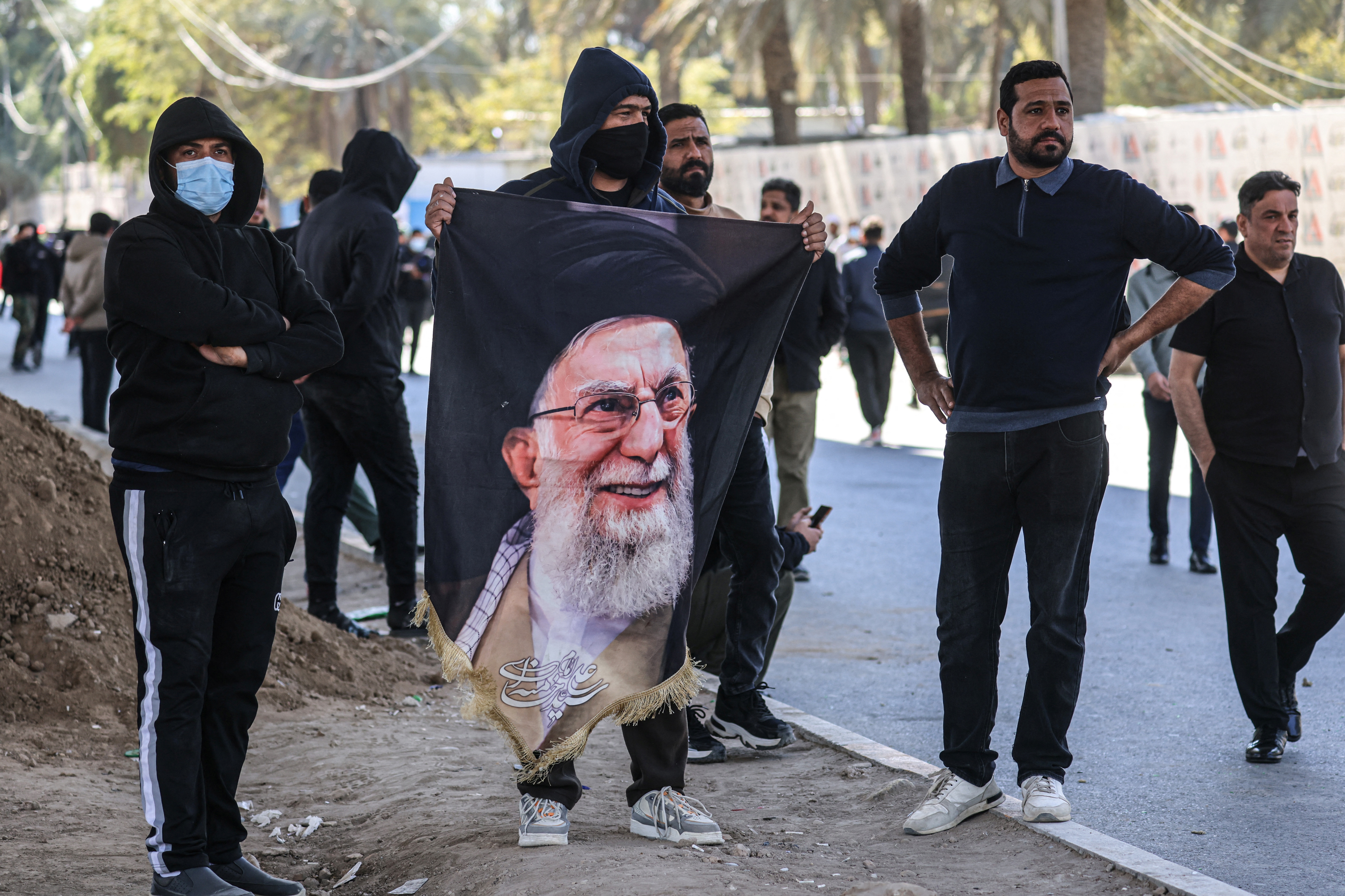Iraqis, one holding a portrait of the assassinated Iranian supreme leader, look on as they try to approach a bridge leading to the Green Zone where the US embassy is located in Baghdad on March 1, 2026, the morning after the US and Israel targeted Iran.