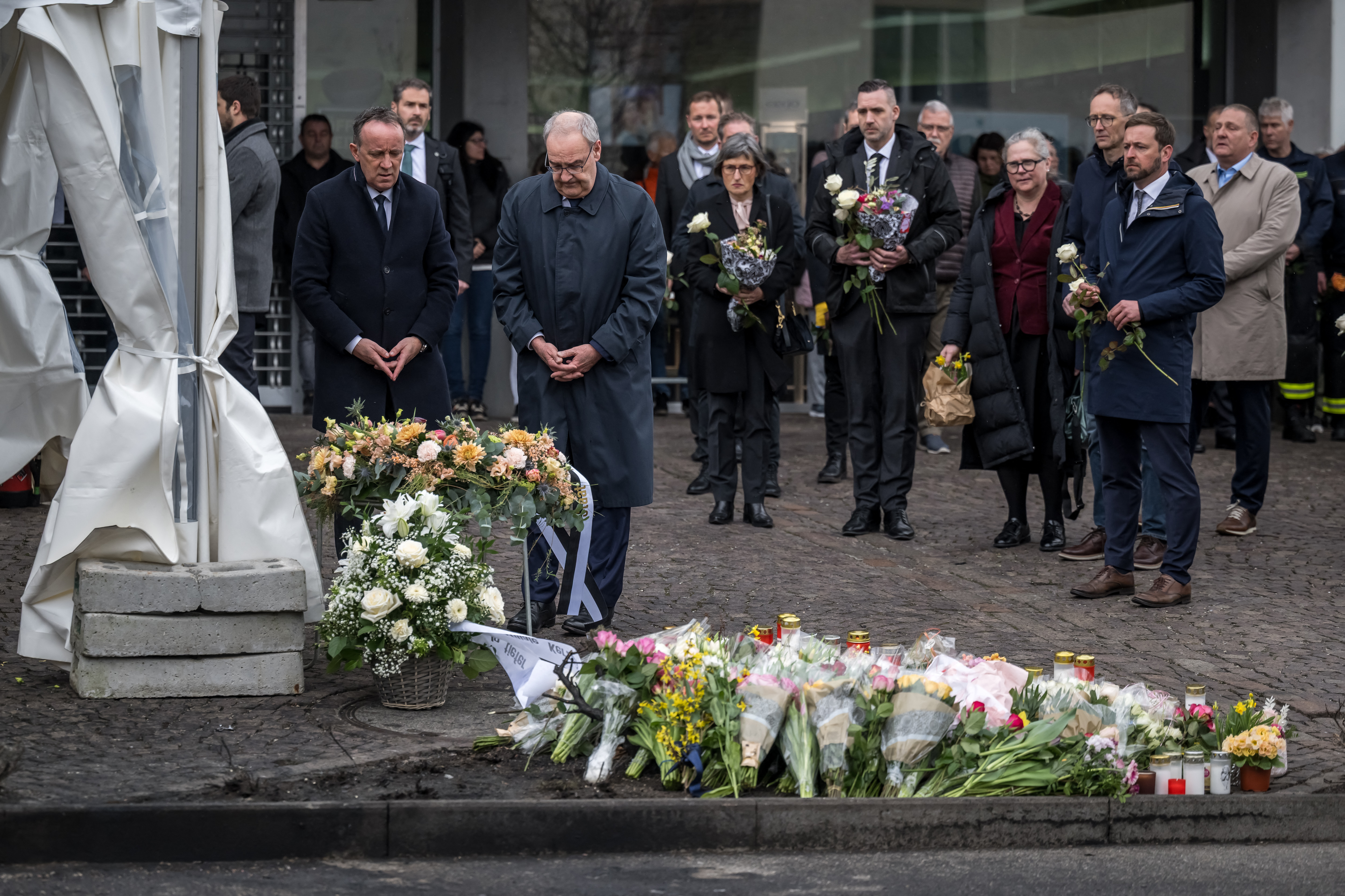 Switzerland's President Guy Parmelin (2nd L) and President of the government of the Canton of Fribourg Philippe Demierre (L) pay their respect during a memorial ceremony in Kerzers, western Switzerland on March 11, 2026, the day after six people were killed in a bus fire which was seemingly started by a disturbed man on board who set himself alight.