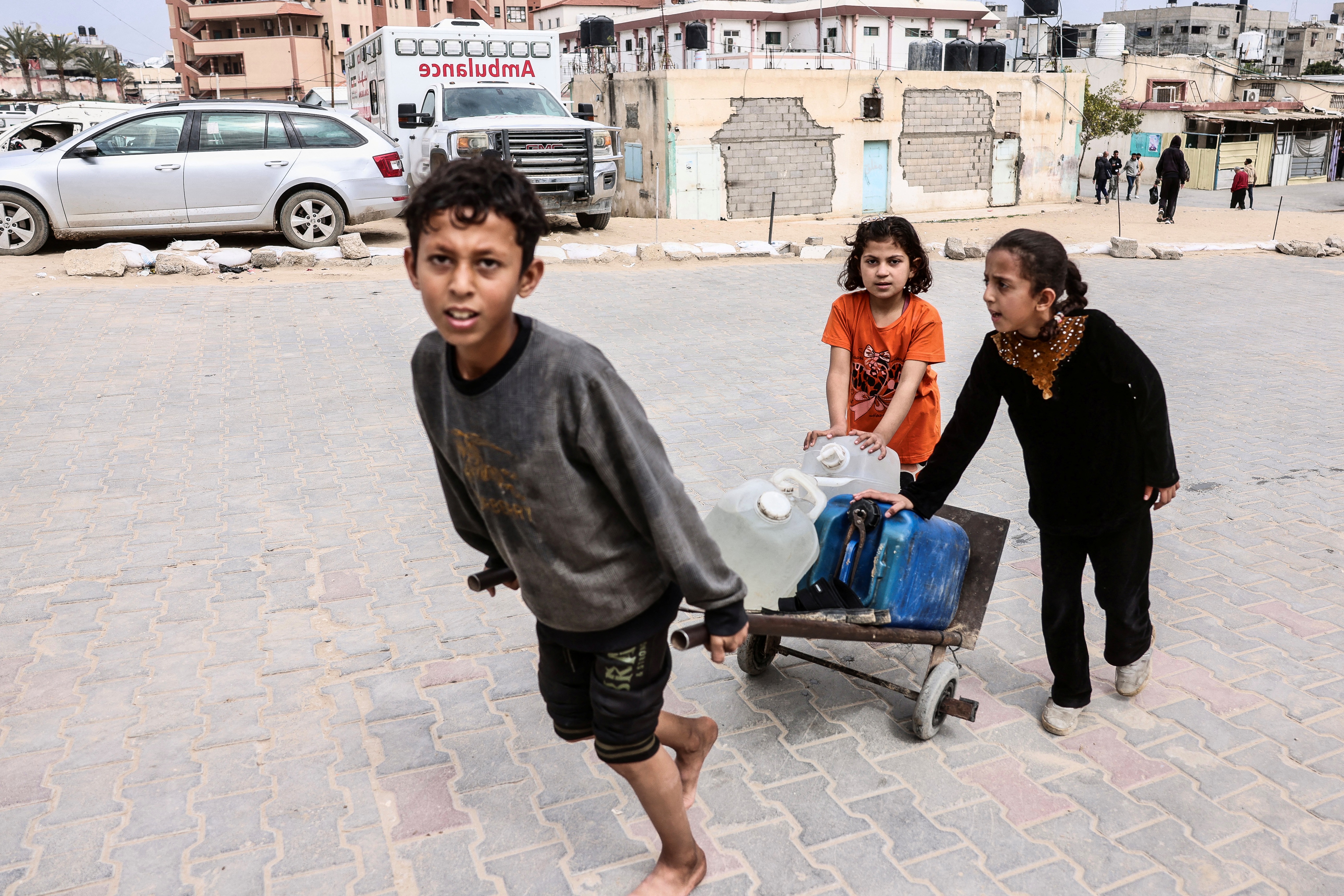 A displaced Palestinian boy pulls a cart with the help of two girls as they transport a water container during the last Friday noon prayer of the Muslim holy fasting month of Ramadan in Khan Yunis, in the southern Gaza Strip on March 13, 2026.