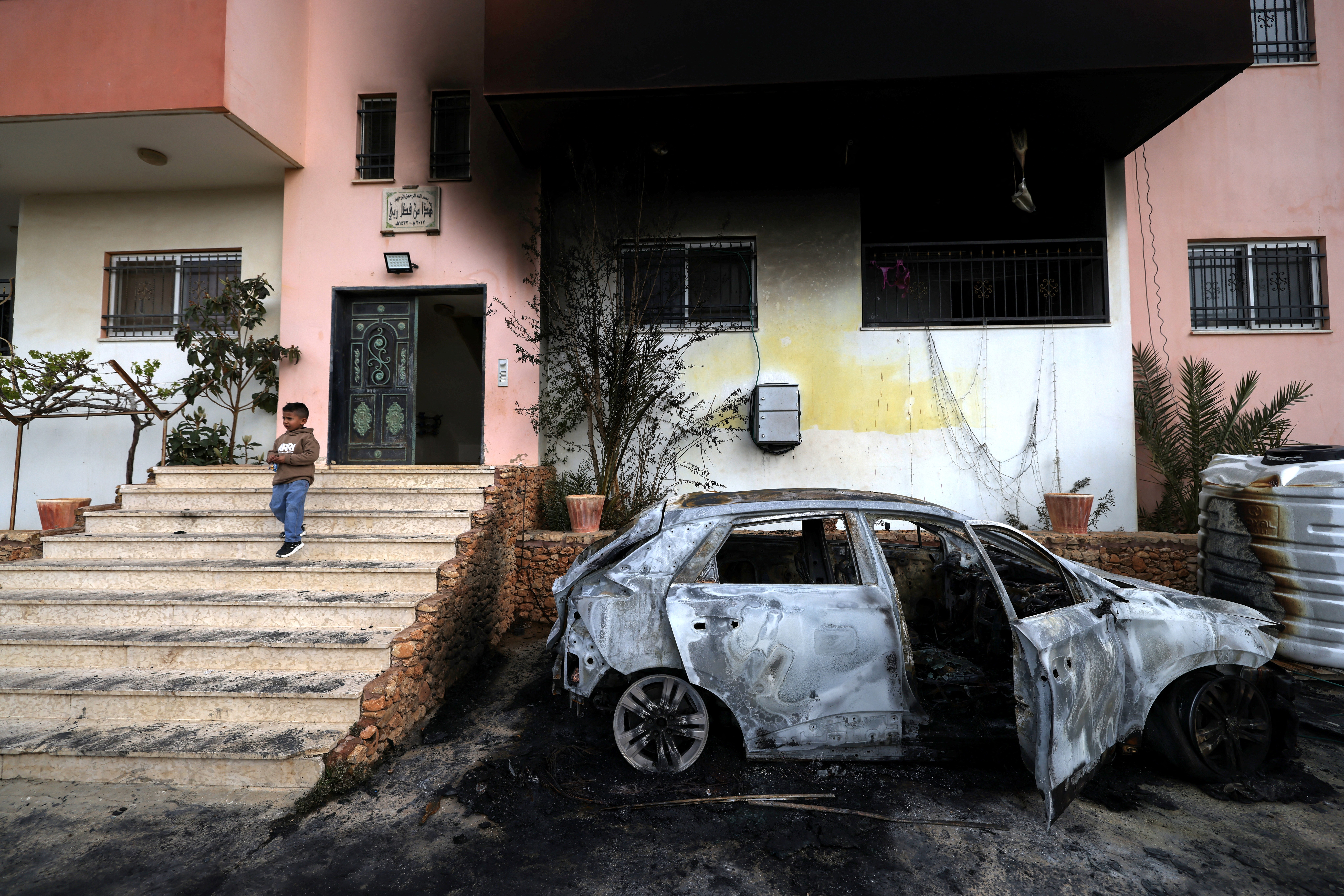 A Palestinian child stands outside a destroyed car and burned-out home.
