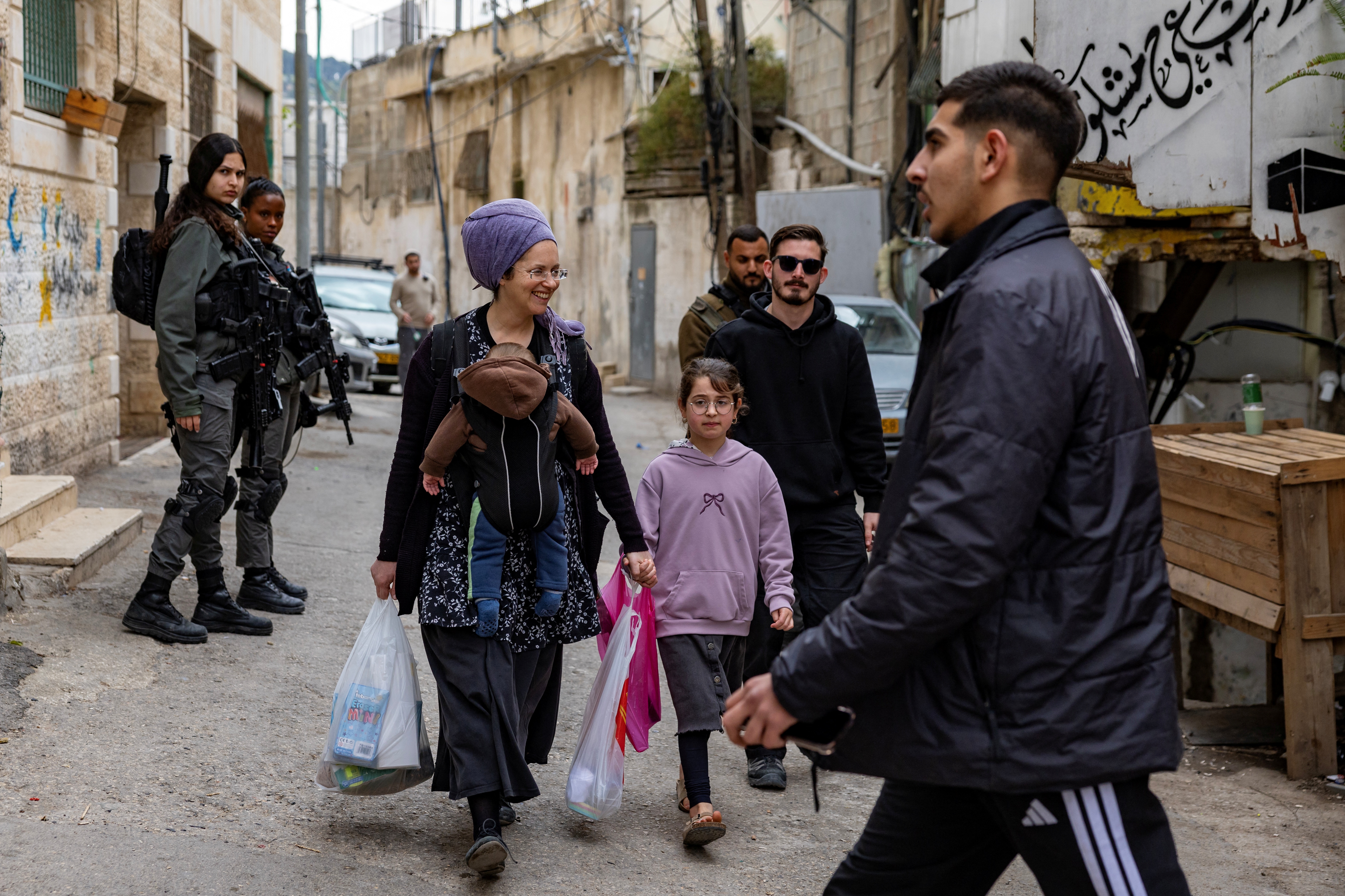 A Palestinian man (R) watch a settler family walking past a group of Israeli police officers as 11 Palestinian families in the Batan al-Hawa area of Silwan are evicted to make room for Israeli settlers, in the predominantly Arab neighbourhood of Silwan in East Jerusalem, on March 25, 2026.