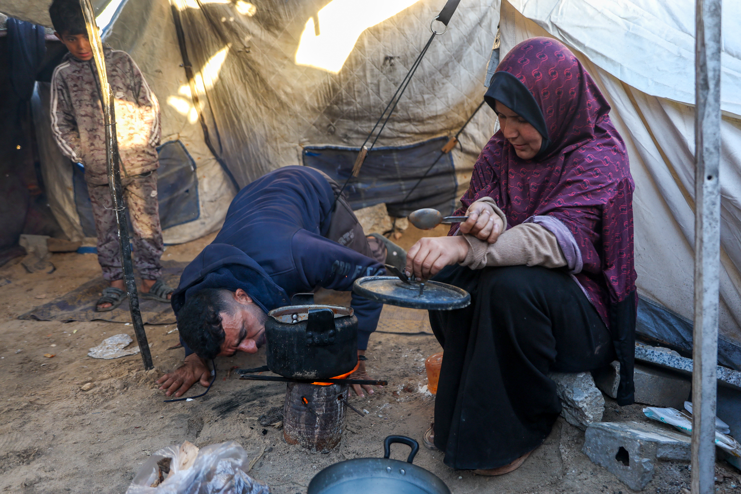 Islam Dardouna and her husband Muath try to ignite a wood fire by blowing on it shortly before preparing their iftar meal during Ramadan