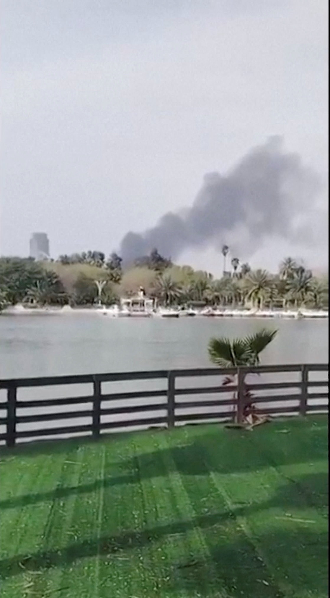 Smoke rises following a reported drone strike near the the Iraqi intelligence headquarters, in Baghdad, Iraq, in this screen grab obtained from social media video released on March 21, 2026. Social Media/via REUTERS THIS IMAGE HAS BEEN SUPPLIED BY A THIRD PARTY. NO RESALES. NO ARCHIVES. VERIFICATION: - Lake, barriers, and tower matched file and satellite imagery - Coordinates of the tower seen in the background: 33.31201658608054, 44.364977341475154 - Exact location hit cannot be confirmed from the video, but the camera appears to be facing towards the Mansour district, where Iraqi officials reported a drone attack on March 21 - Exact date not verified but no older version of the video was found posted online before March 21 - The National Intelligence Service also said an officer was killed after a drone launched by "outlaw groups" struck near the Iraqi intelligence headquarters in Baghdad on March 21