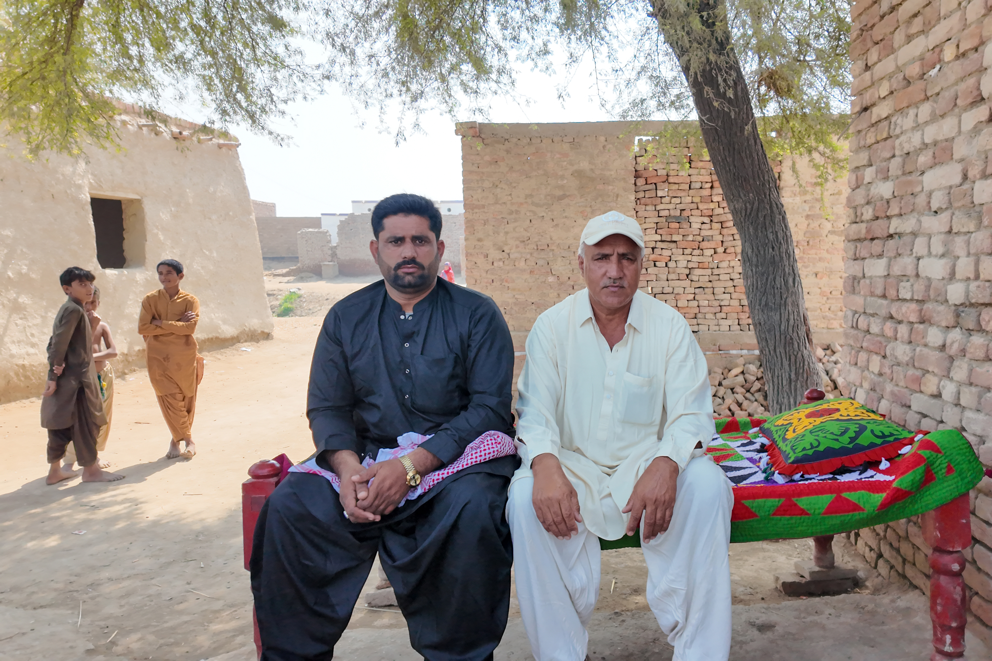 Two men sit in front of bare stone houses.